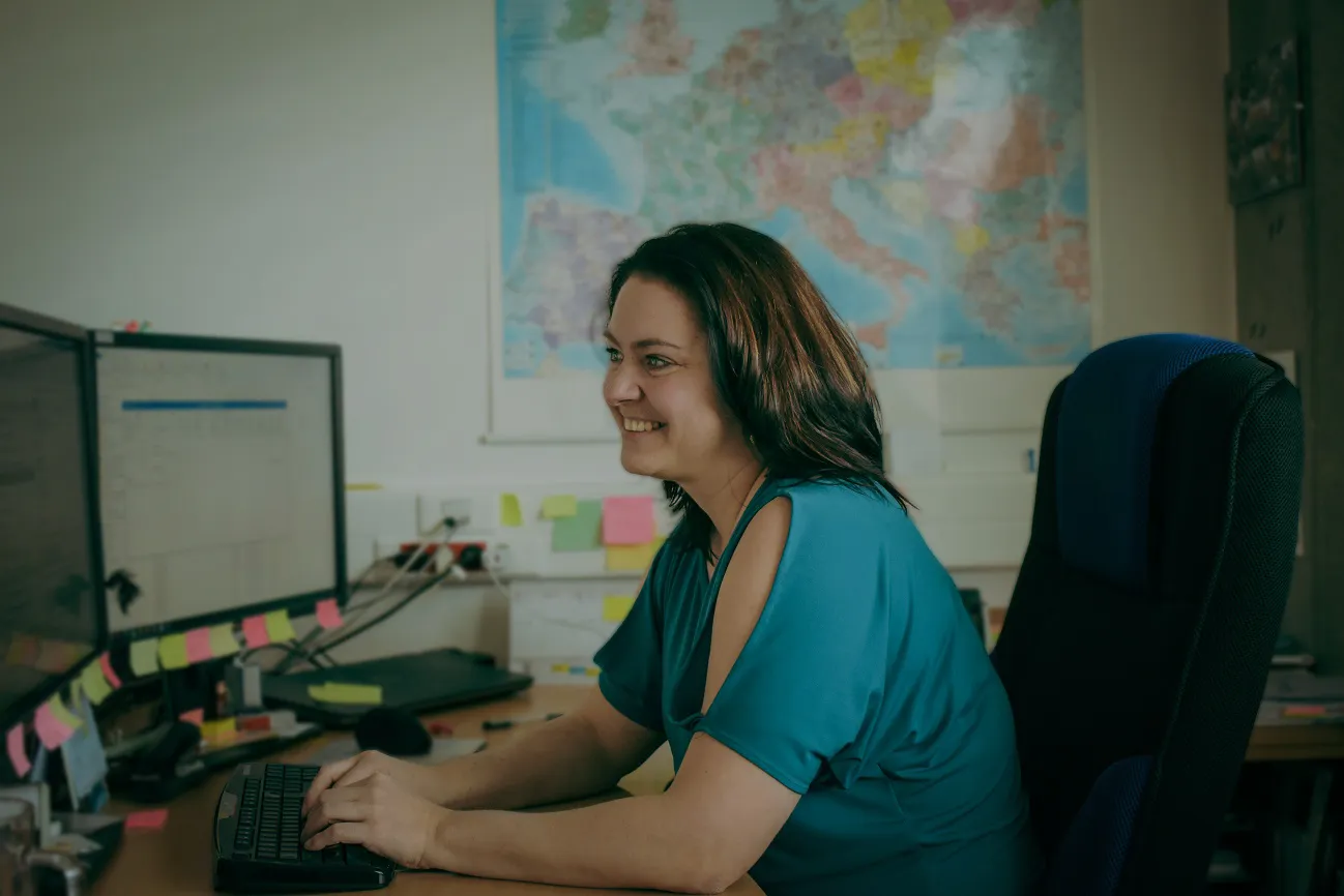 Ein lächelnder Mann in einem Serverraum hält einen Laptop in der Hand.