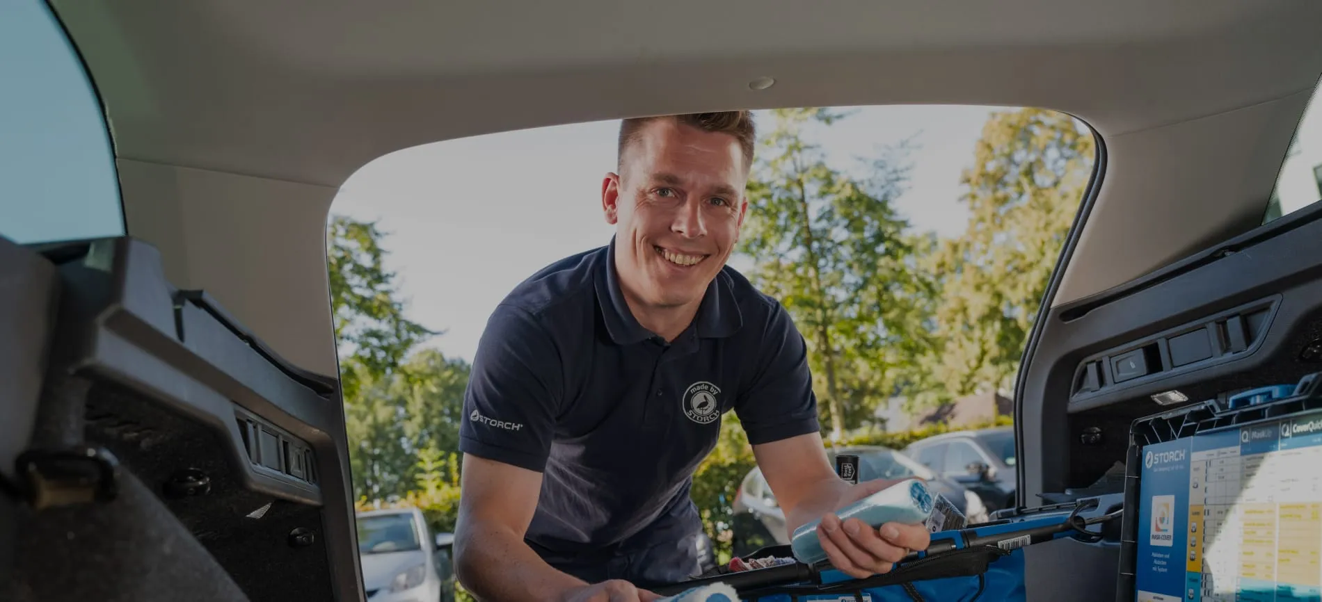 Ein lächelnder Mitarbeiter lädt Malerutensilien in den Kofferraum eines Autos.
