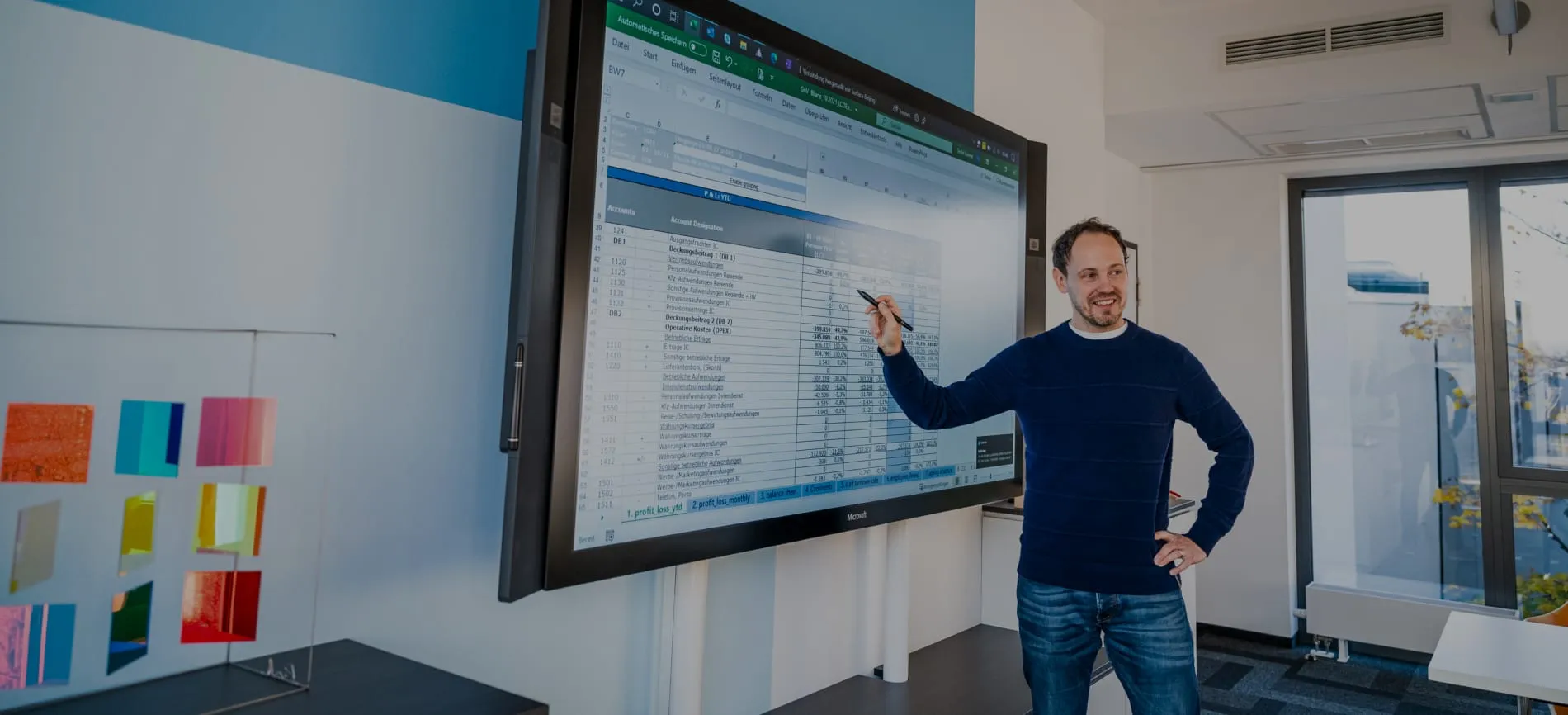 Ein Mann präsentiert ein Excel-Dokument auf einem großen Bildschirm in einem modernen Büro.