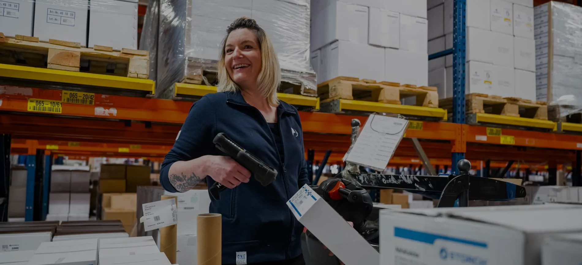 Eine Mitarbeiterin im Lager von Storch-Ciret Business Services GmbH, lächelnd mit einem Scanner in der Hand.