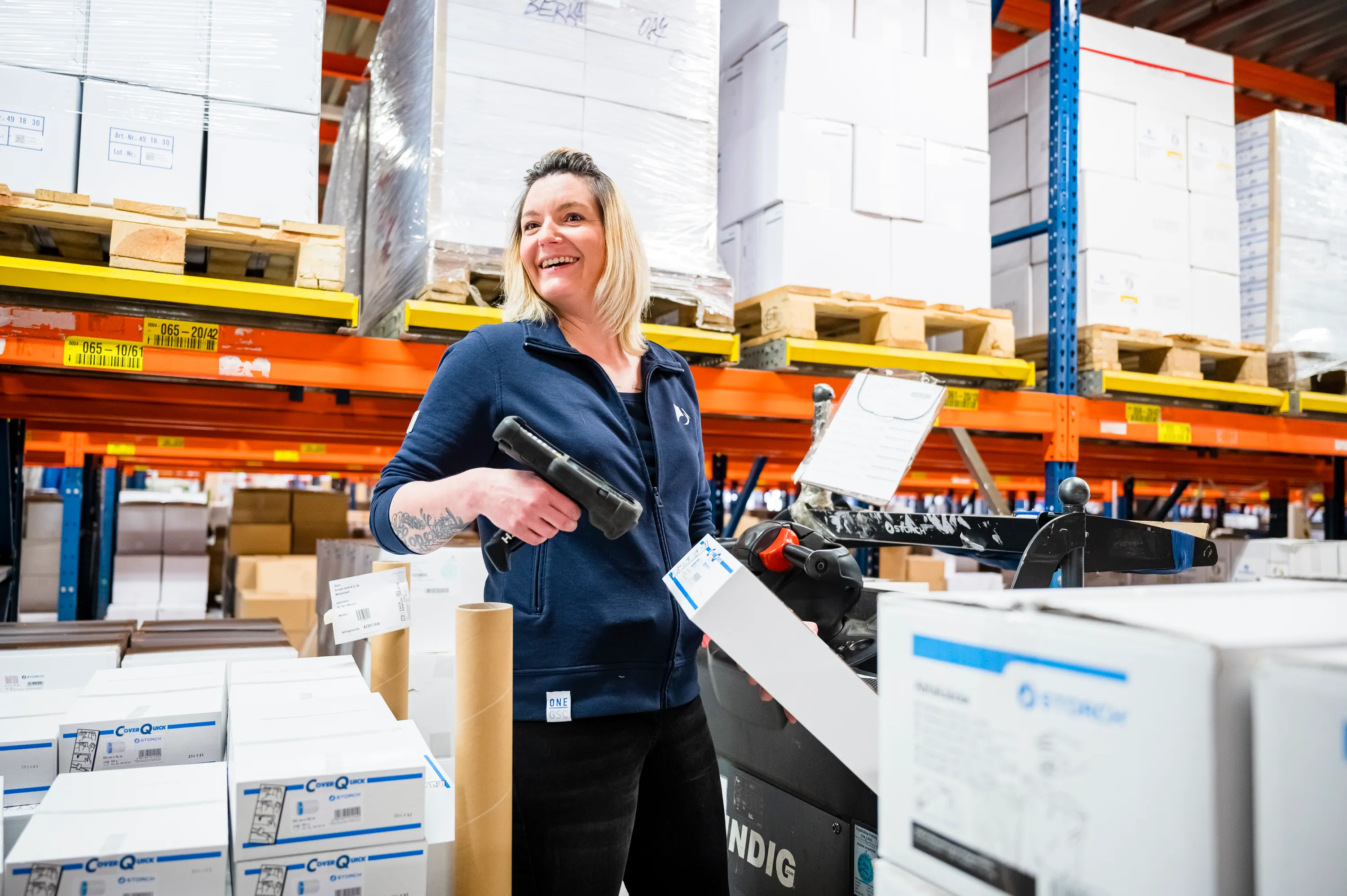 Eine Mitarbeiterin im Lager von Storch-Ciret Business Services GmbH, lächelnd mit einem Scanner in der Hand.
