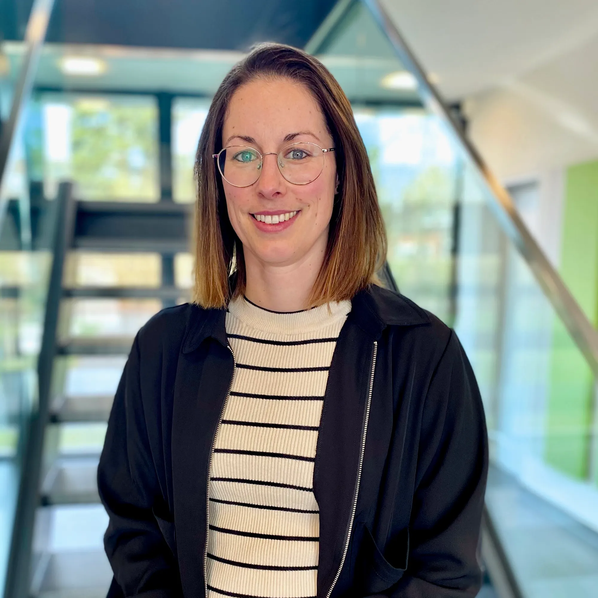 Junge Frau mit Brille lächelt freundlich in einem modernen Bürogebäude, ideal für Deine Karriere im Food & Beverage Bereich.
