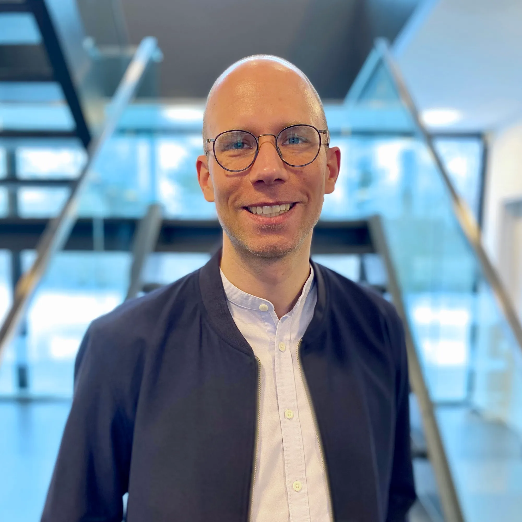 Lächelnder Mann mit Brille in moderner Büroumgebung, bereit für Deine Karriere im Food-and-Beverage-Bereich.