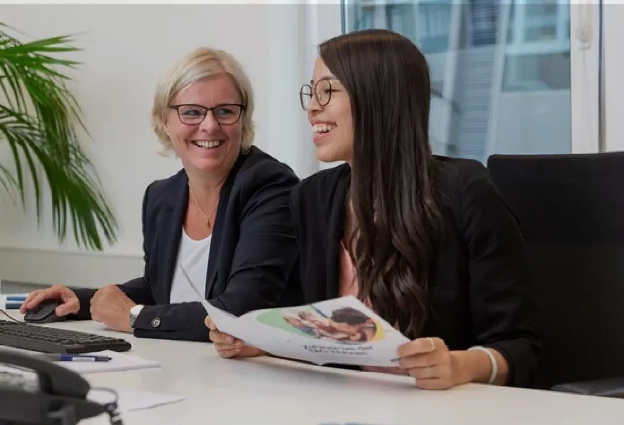 Zwei lächelnde Mitarbeiterinnen in einem modernen Büro bei TAG Immobilien AG, die ein Dokument besprechen.