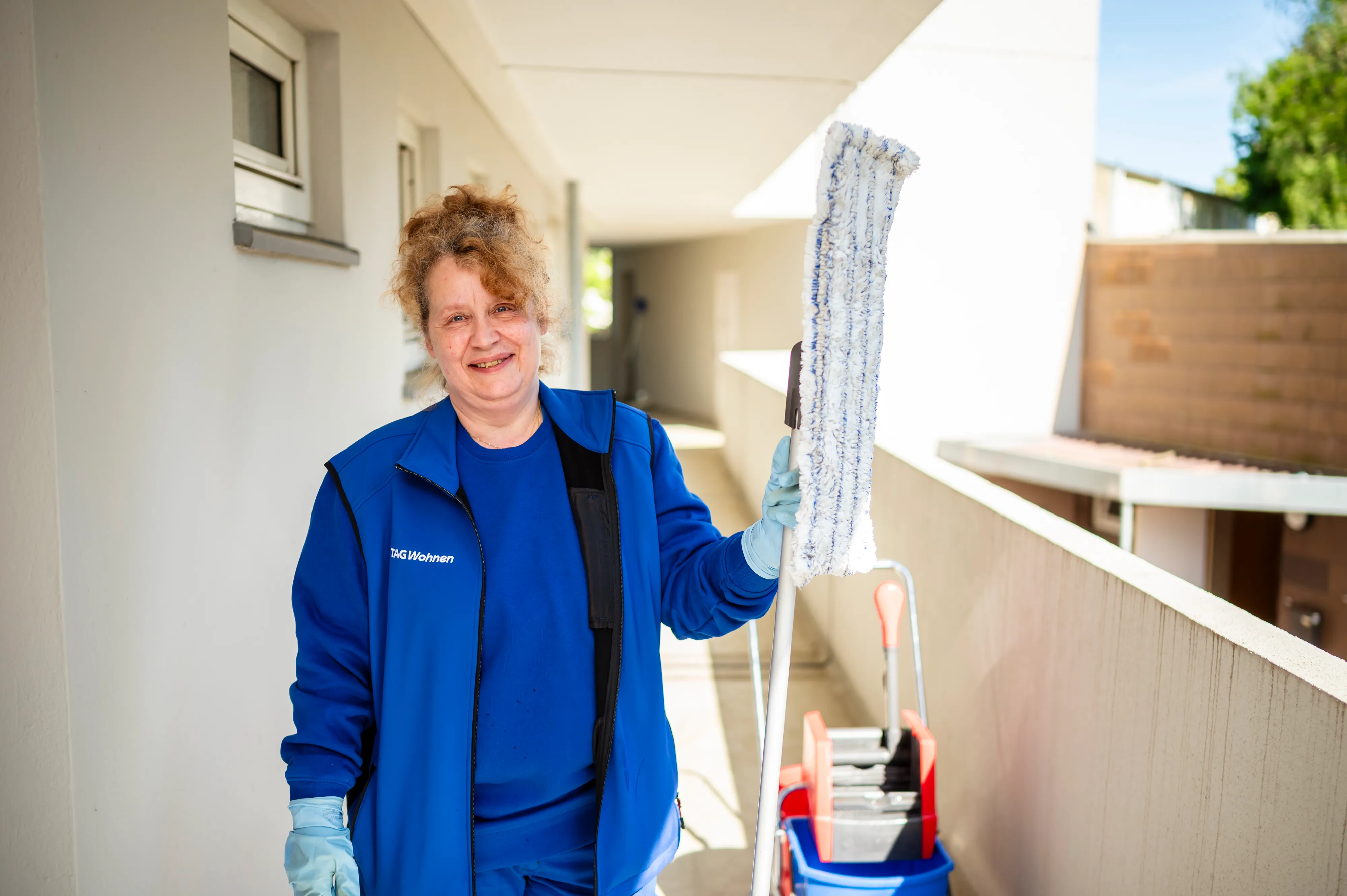 Drei Hausmeister in blauer Arbeitskleidung stehen im Freien neben einem Aufsitzrasenmäher.