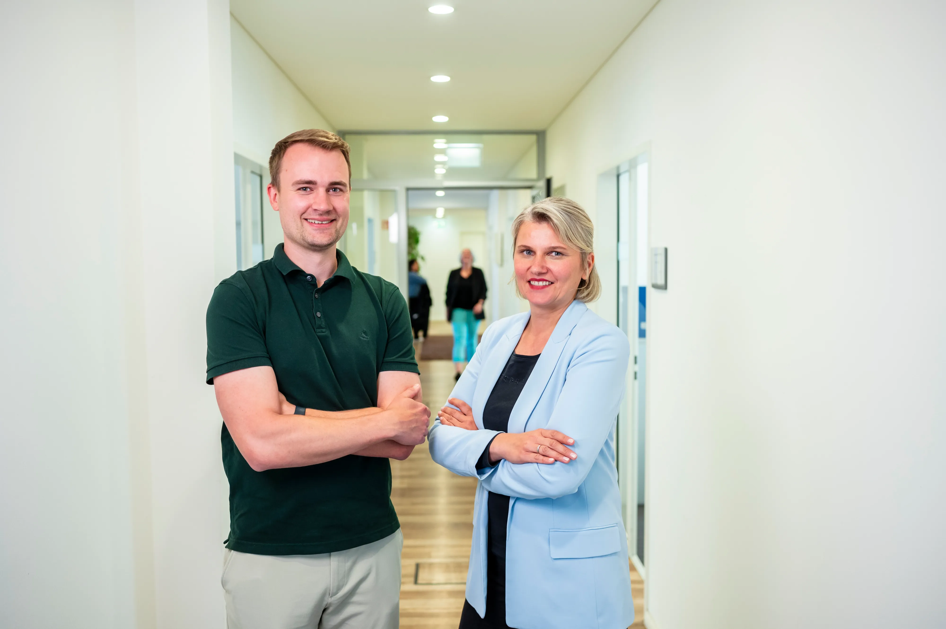 Ein Mitarbeiter lächelt in die Kamera an der Rezeption von TAG Immobilien AG, während Kollegen im Hintergrund plaudern.