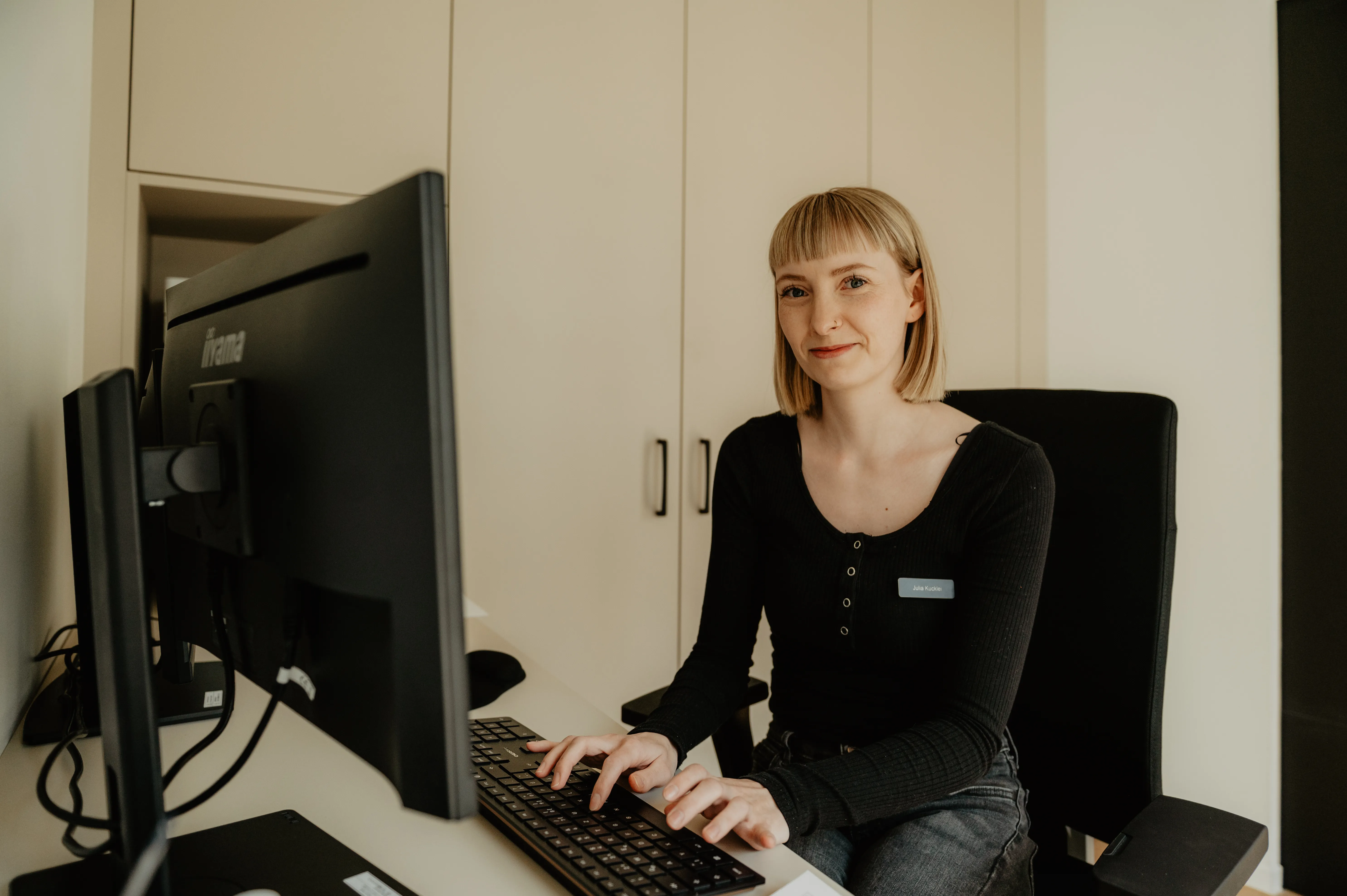 Eine Zahmedizinische Verwaltungsassistenz sitzt am Schreibtisch und tippt auf der Tastatur in einer Zahnarztpraxis.