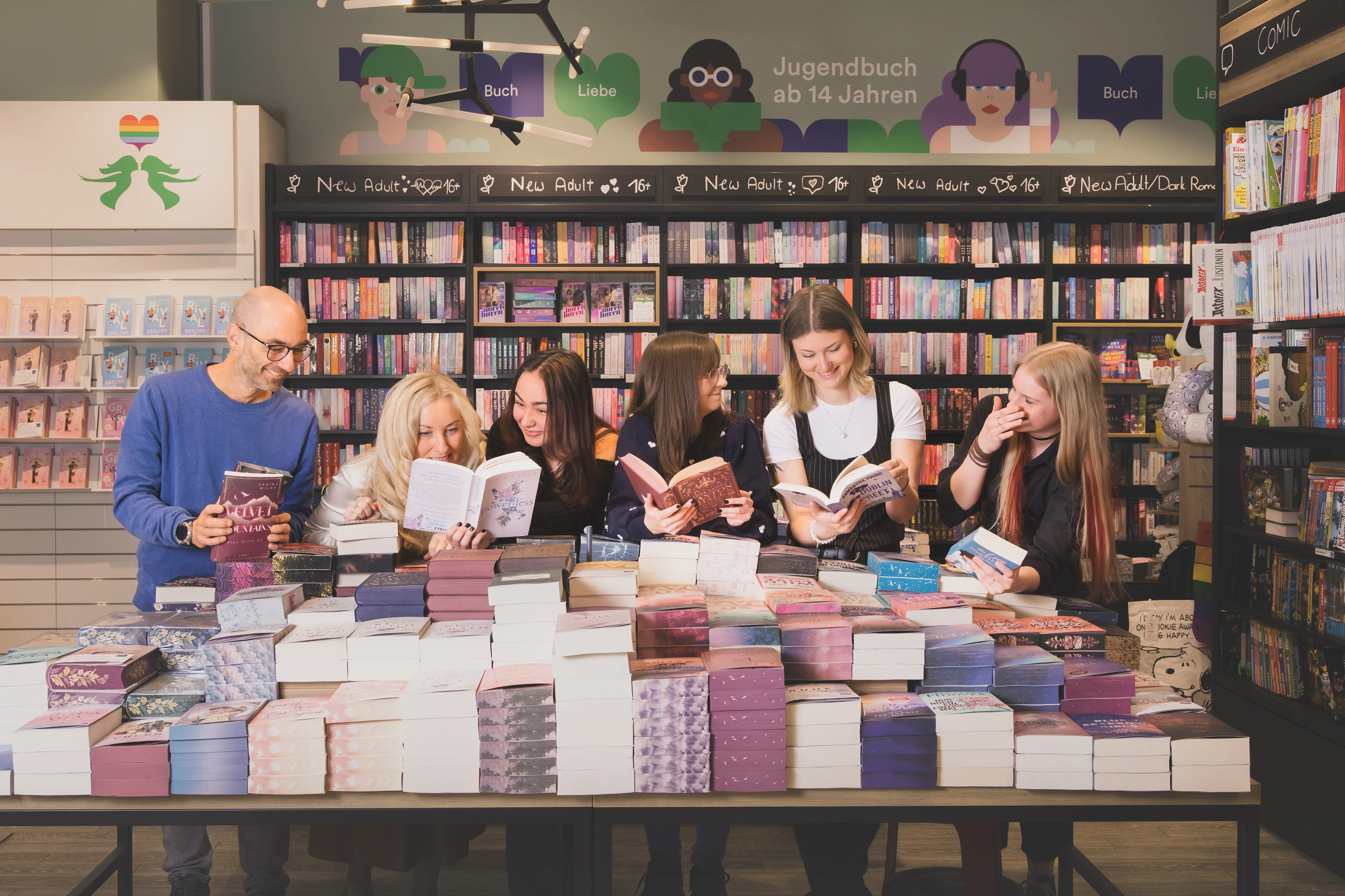 Sechs junge Menschen stöbern gemeinsam in Büchern bei Thalia, umgeben von bunten Buchregalen und gemütlicher Atmosphäre.