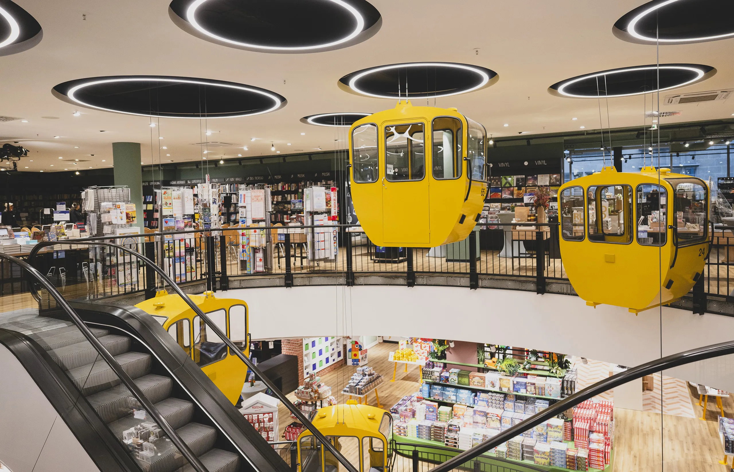 Eine moderne Buchhandlung mit gelben Gondeln, Rolltreppe und Bücherregalen bei Thalia Bücher GmbH.
