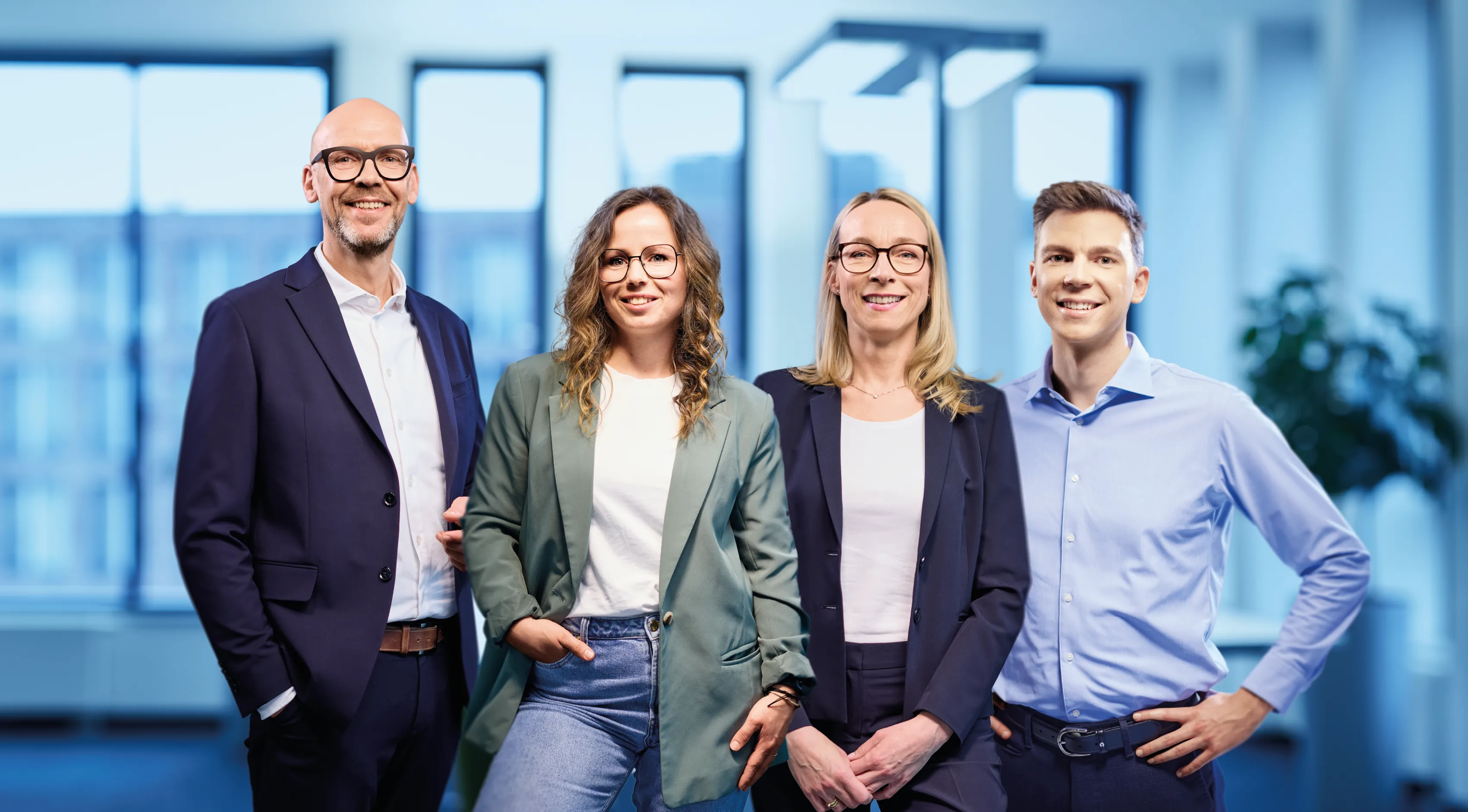 Vier freundliche Thyssengas-Mitarbeitende stehen gemeinsam in einem modernen Büro und lächeln Dich direkt an.