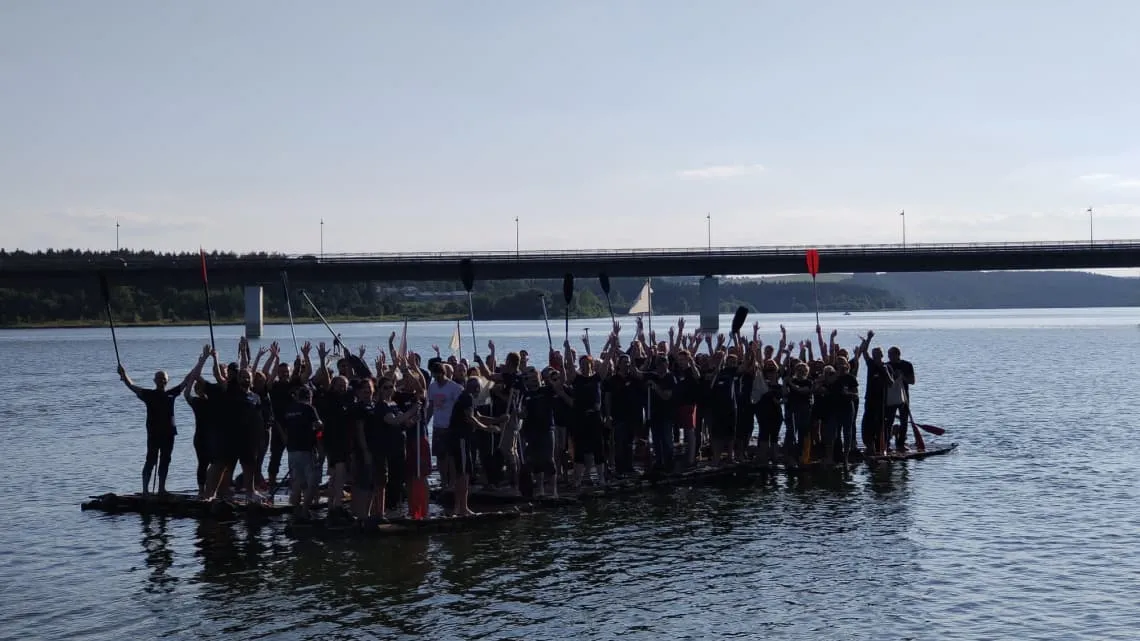 Große Gruppe von TIMAC AGRO Mitarbeitenden steht gemeinsam auf einem Floß und feiert Teamgeist auf dem Wasser.
