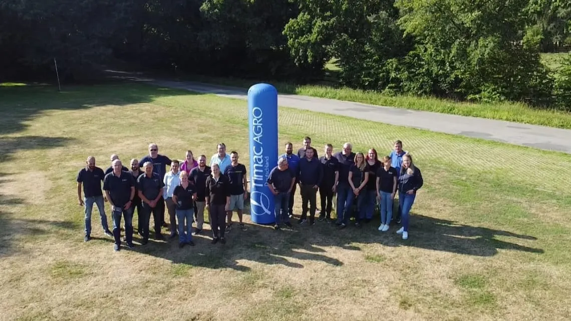 Eine Gruppe von TIMAC AGRO Deutschland Mitarbeitenden steht gemeinsam draußen neben einer blauen Firmen-Säule.