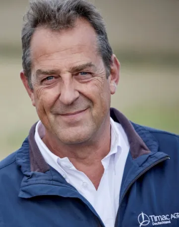 Ein freundlicher Mitarbeiter von TIMAC AGRO Deutschland lächelt direkt in die Kamera und trägt eine Firmenjacke.