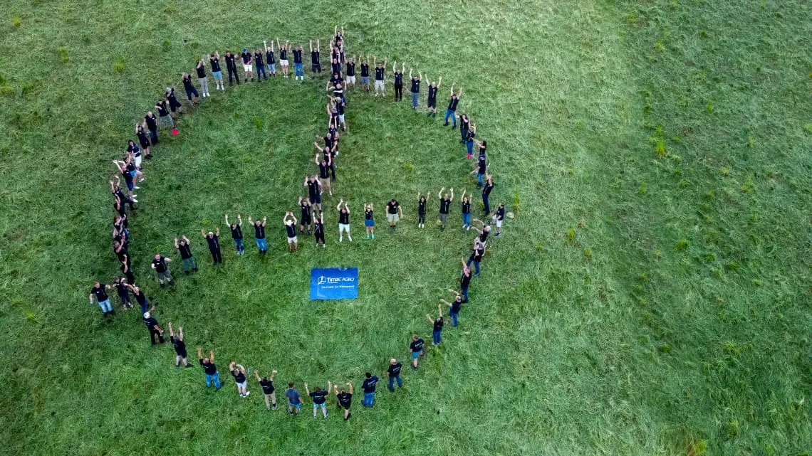 Mitarbeitende von TIMAC AGRO formen auf einer Wiese gemeinsam ein Peace-Zeichen und zeigen Teamgeist.