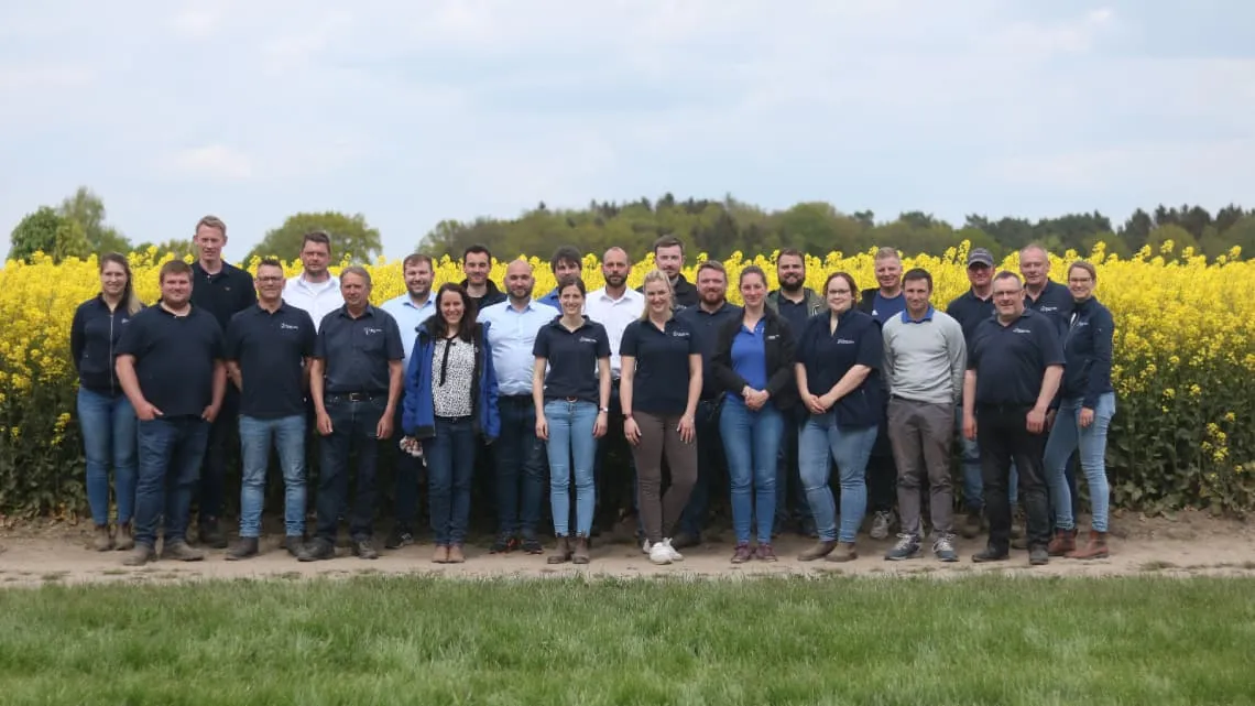 Das Team von TIMAC AGRO Deutschland steht gemeinsam vor einem blühenden Rapsfeld und lächelt in die Kamera.