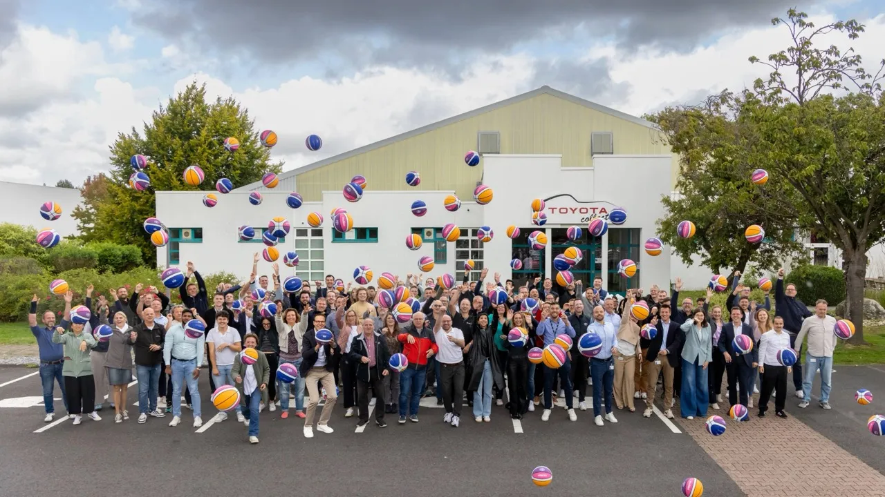 Großes, fröhliches Team von Toyota Deutschland wirft bunte Bälle vor dem Firmengebäude in die Luft.