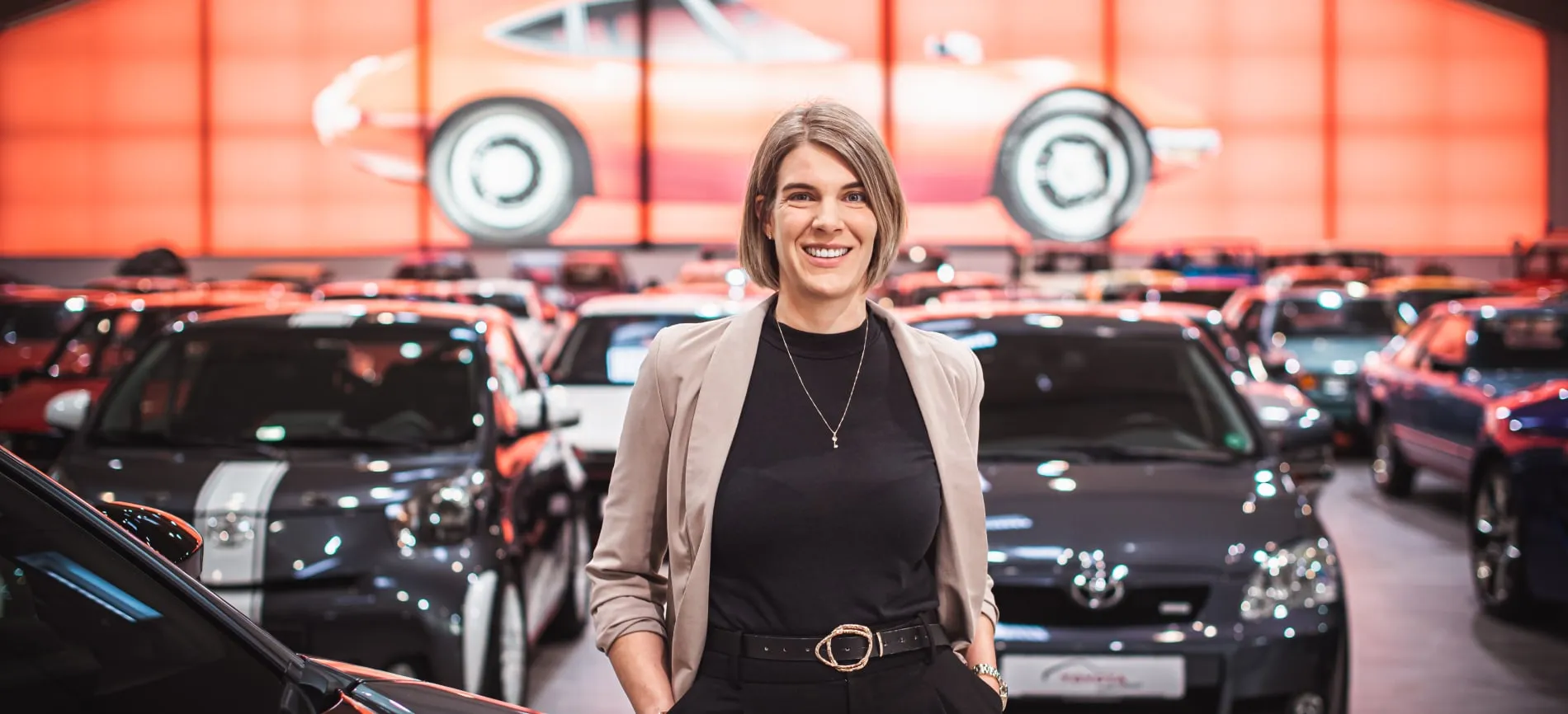 Junge Frau lächelt im Autohaus von Toyota, umgeben von Fahrzeugen, motiviert dich für deine Karriere im Automobilbereich.