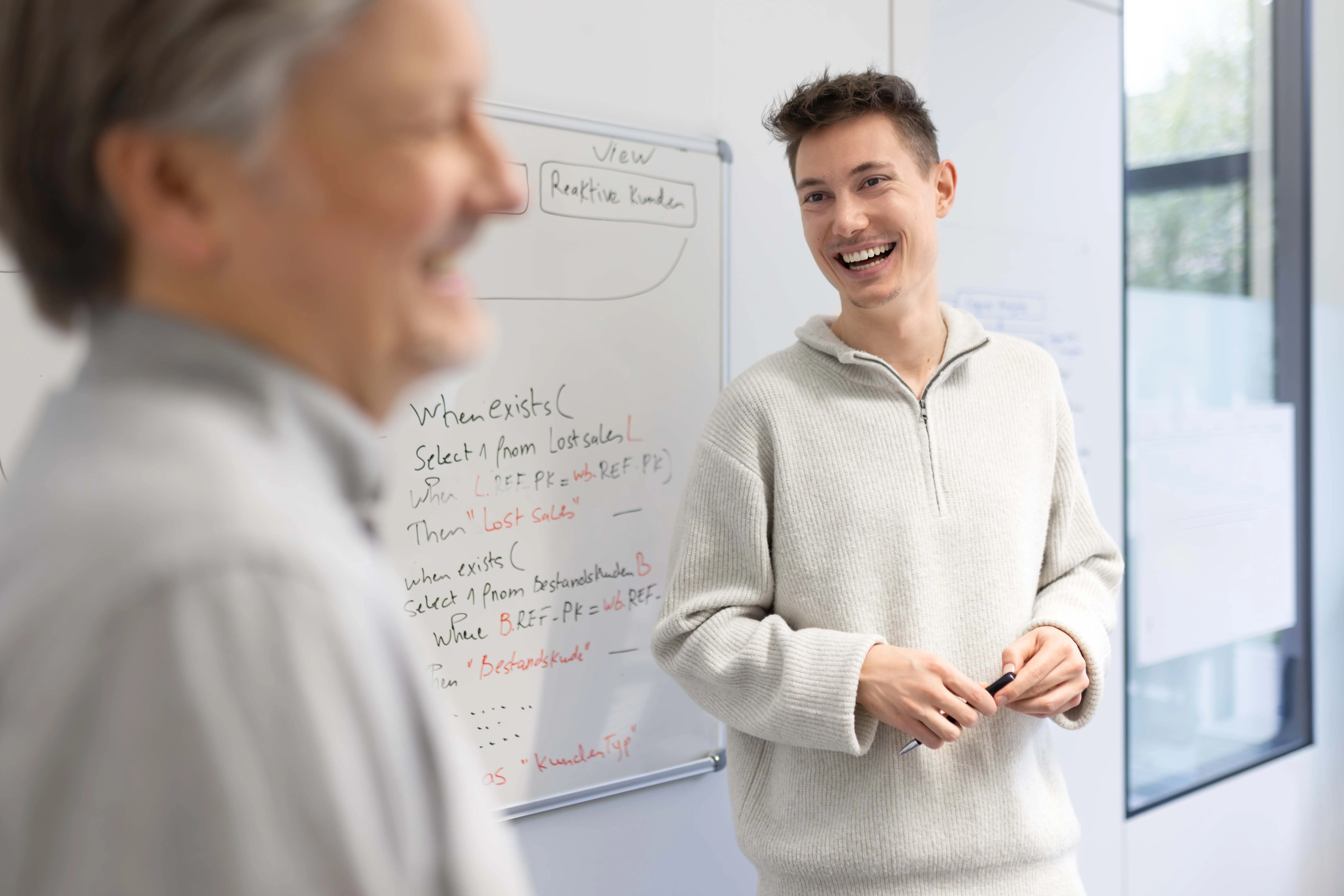 Zwei Kollegen im Gespräch vor einem Whiteboard im Büro, lockere Atmosphäre bei TSR Group.
