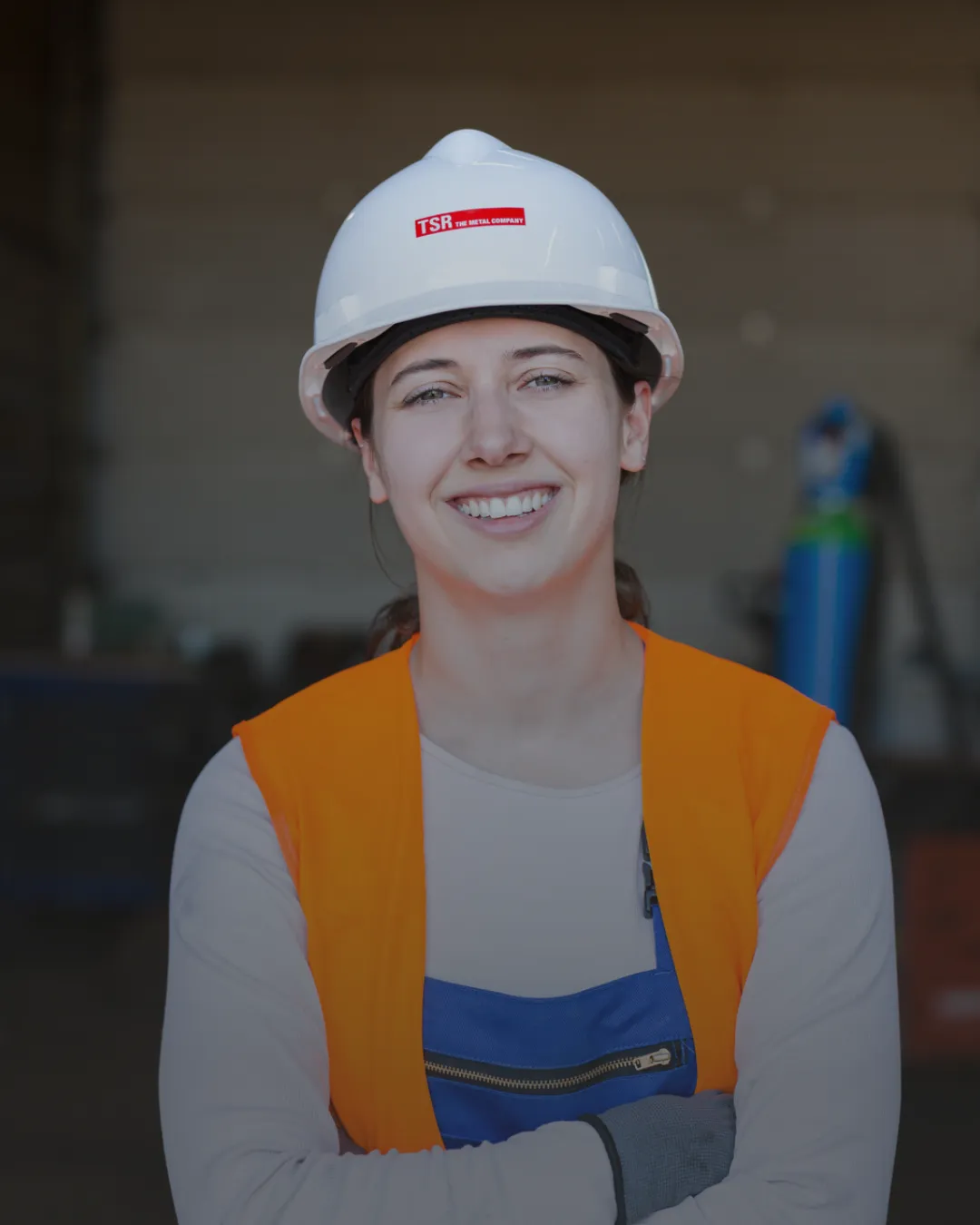 Junge Frau mit Schutzhelm und Warnweste lächelt in einer Werkshalle bei TSR Group GmbH & Co. KG.