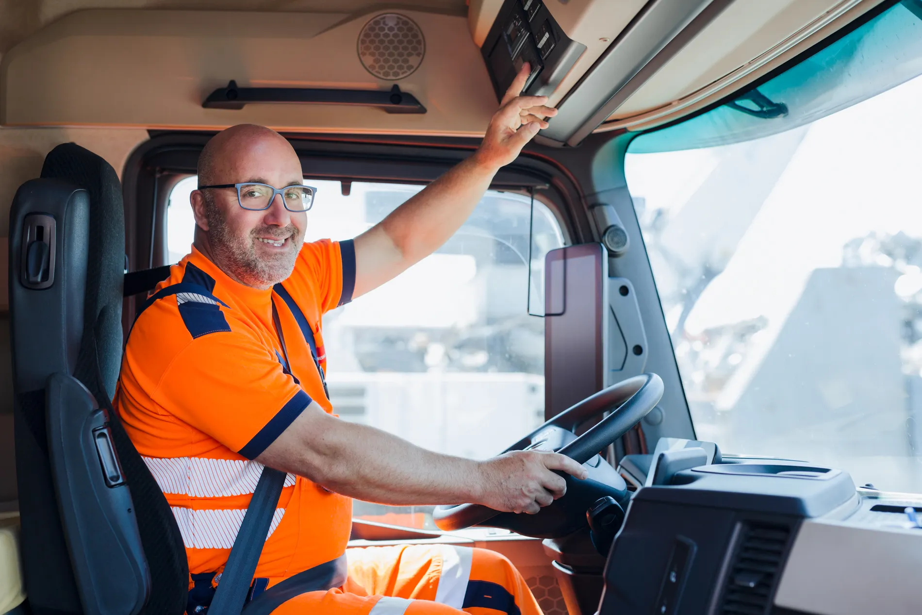 Lächelnder Fahrer in orangefarbener Arbeitskleidung sitzt im LKW bei TSR Group.
