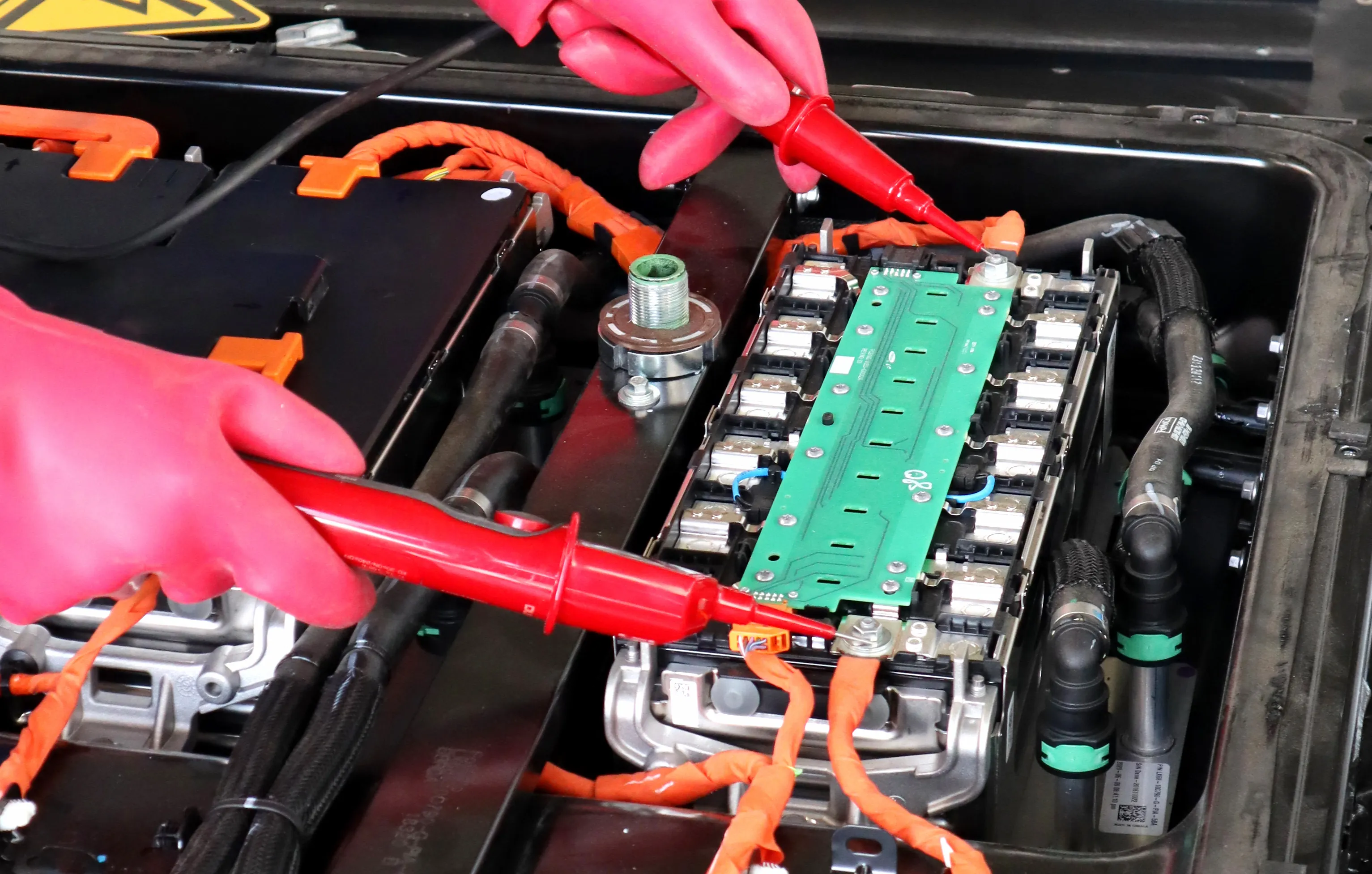 Du prüfst mit Messgeräten und Schutzhandschuhen eine Batterieeinheit.