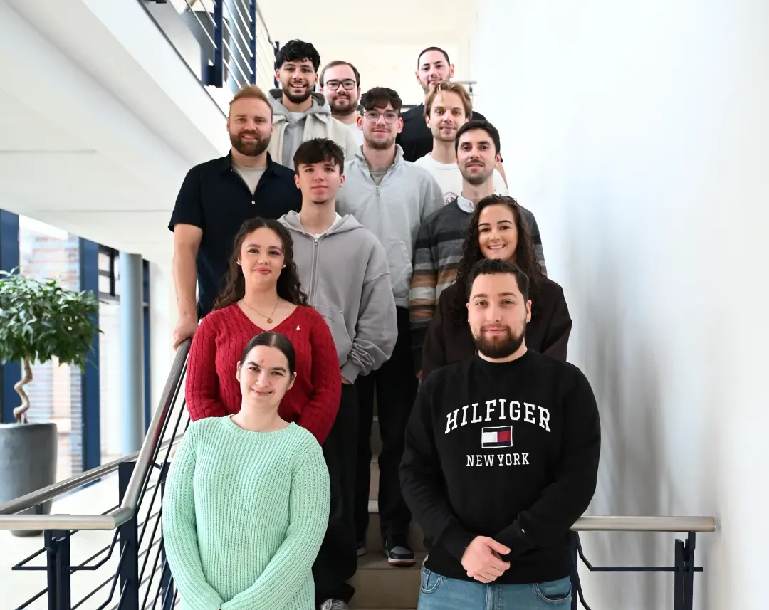 Eine Gruppe Azubis von TSR Group steht freundlich lächelnd gemeinsam auf einer Treppe im Bürogebäude.