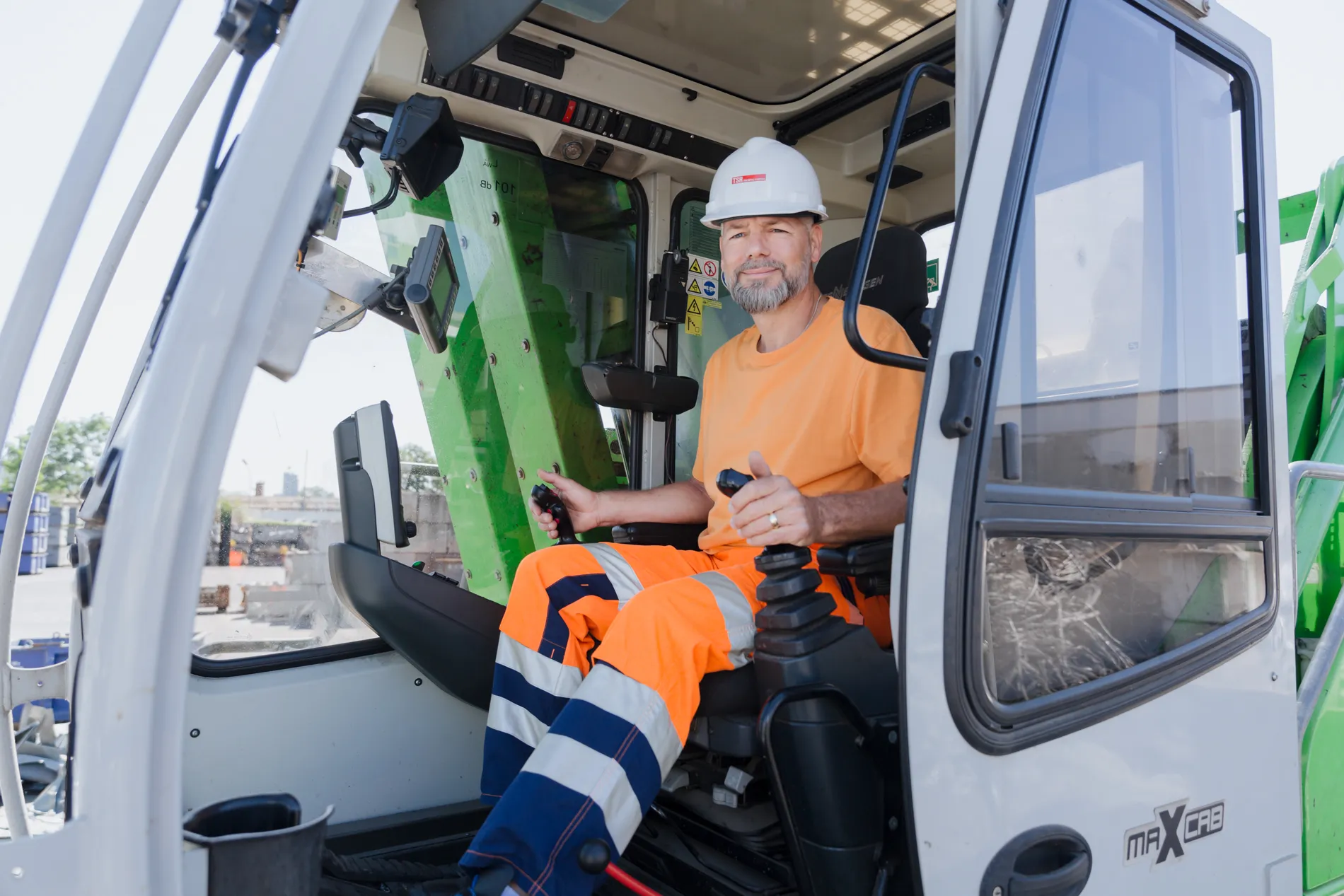 Ein Mitarbeiter sitzt in der Fahrerkabine eines Baggers und lächelt in die Kamera. 