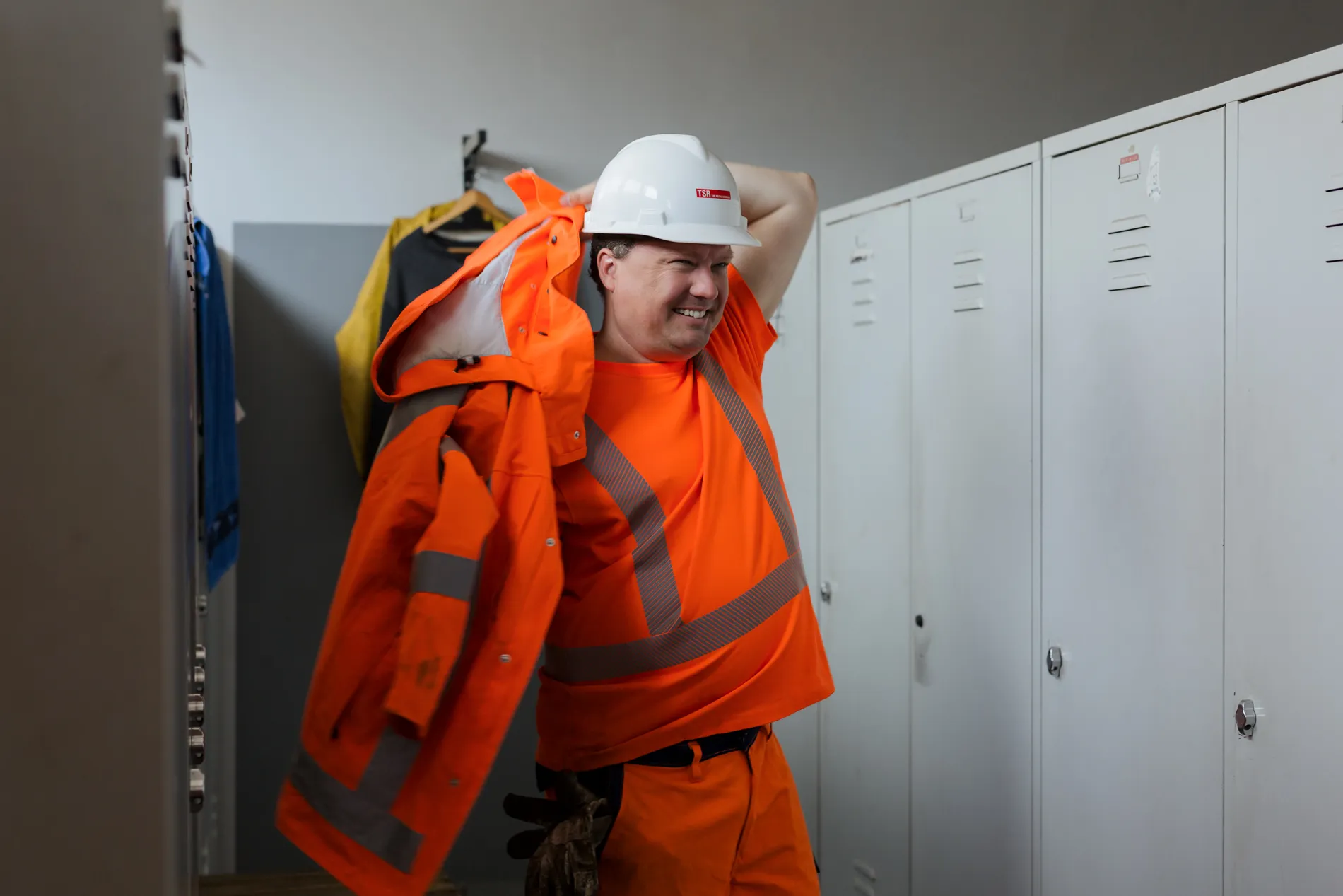 Ein Mitarbeiter zieht im Umkleideraum seine orange Schutzkleidung und einen Helm von TSR Group an – bereit für den Einsatz.