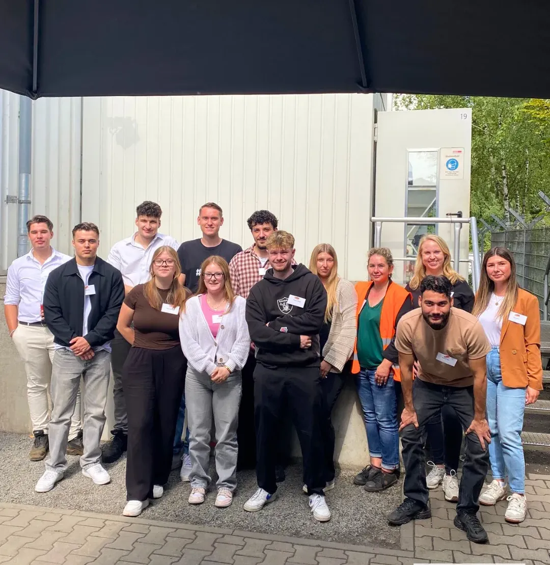 Eine Gruppe junger Mitarbeitender und Auszubildender von TSR Group posiert gemeinsam draußen vor einem Firmengebäude.