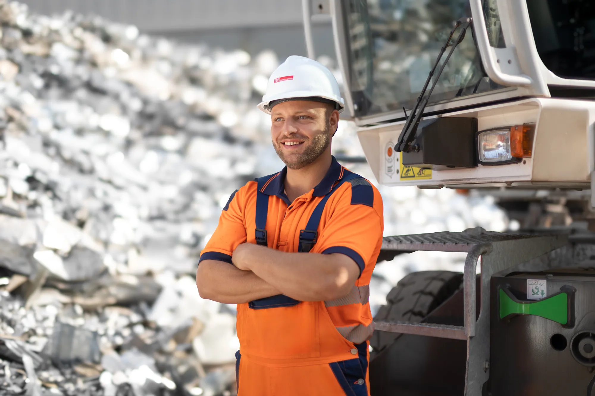 Lächelnder Mitarbeiter in orangefarbener Arbeitskleidung und Helm steht vor einem Bagger bei TSR.