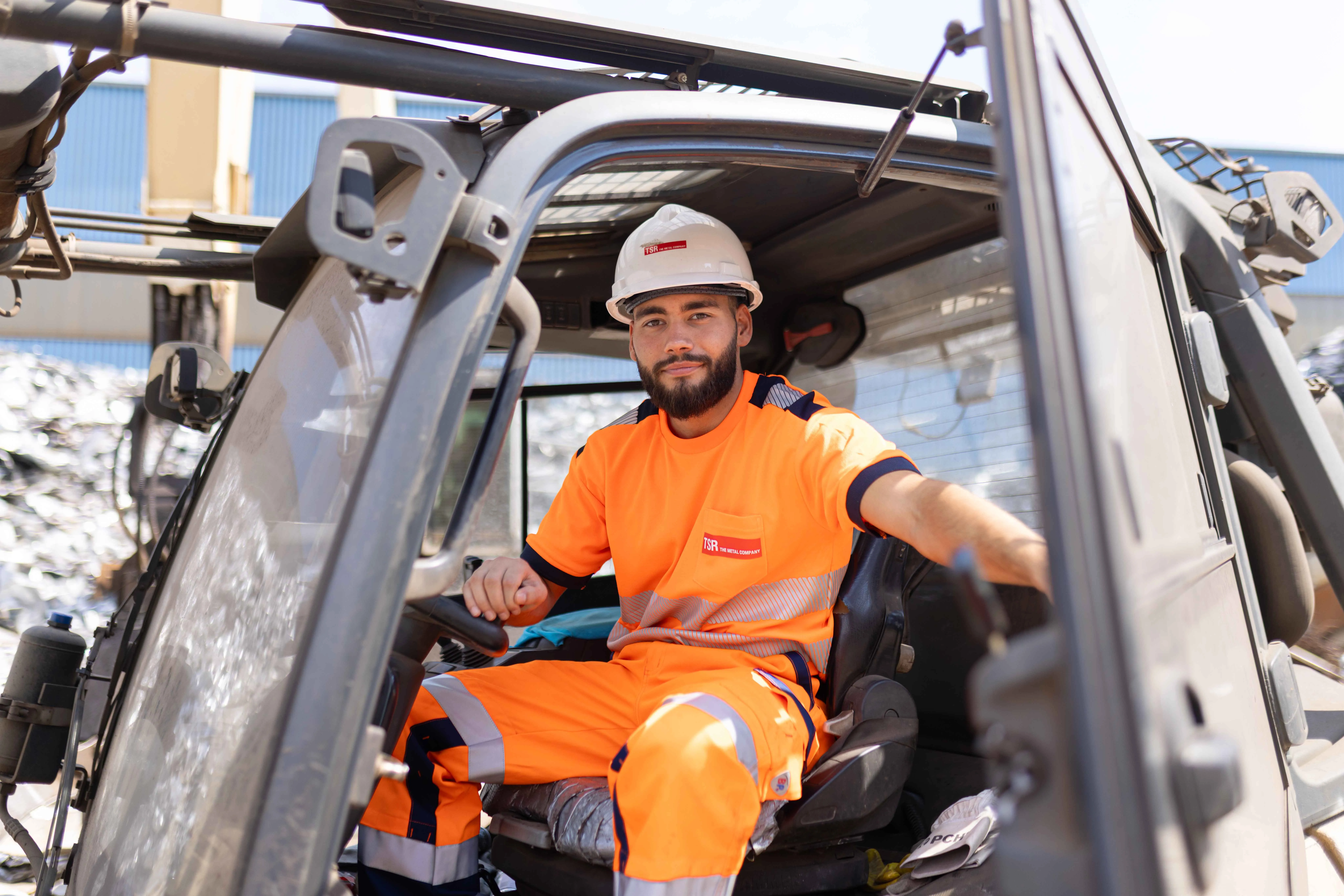 Azubi in orangefarbener Schutzkleidung und Helm sitzt in einem Fahrzeug auf dem TSR-Gelände.