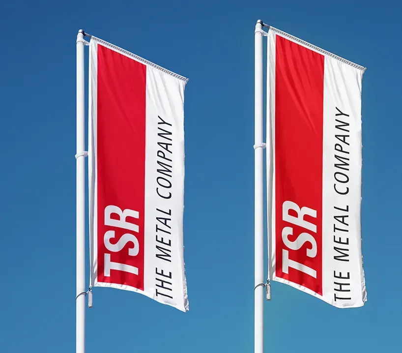 Zwei Fahnen mit TSR-Logo und dem Schriftzug "The Metal Company" vor blauem Himmel. 