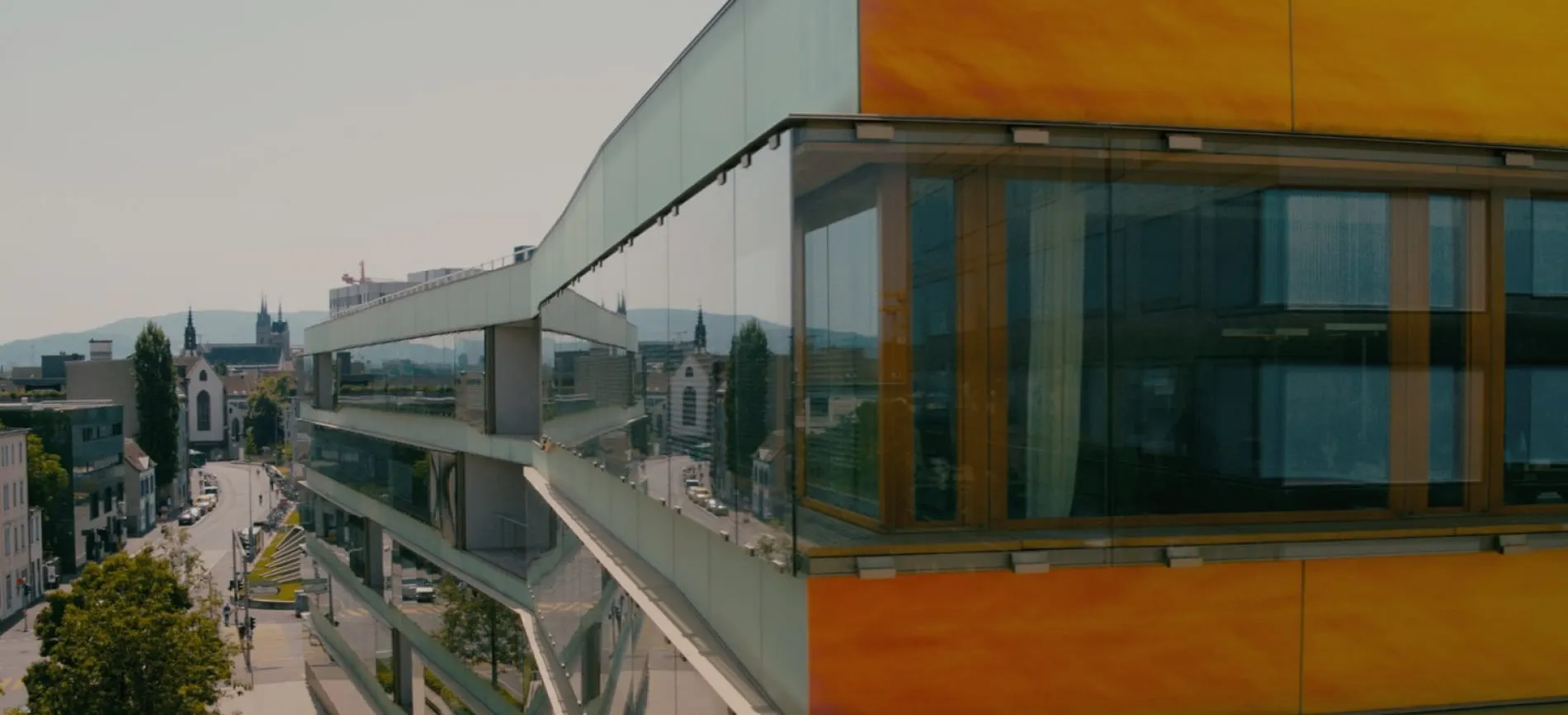 Moderne Glasfassade des UKBB-Gebäudes mit Blick auf die Stadt Basel und umliegende Architektur.