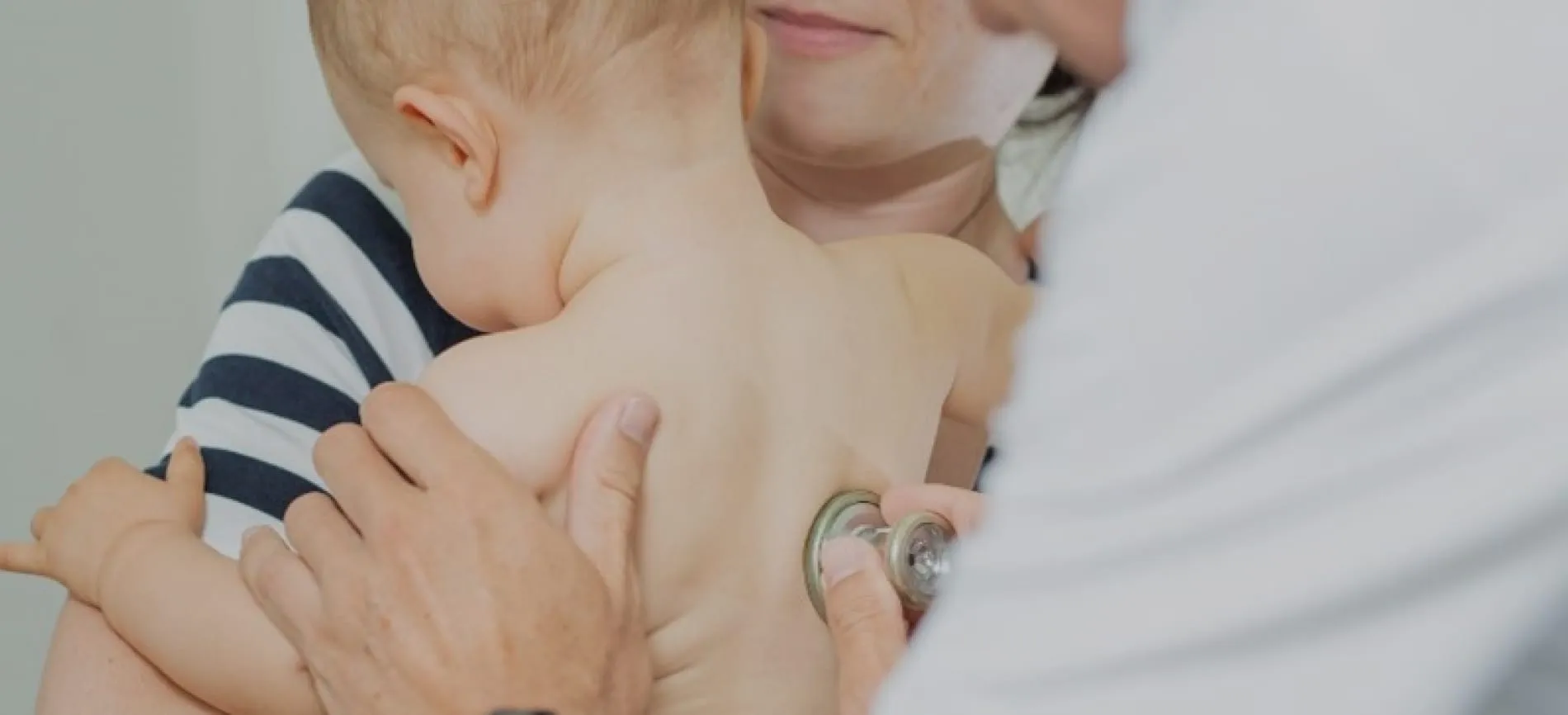 Eine Ärztin hört bei einem Baby, das auf dem Arm gehalten wird, mit dem Stethoskop den Rücken ab.