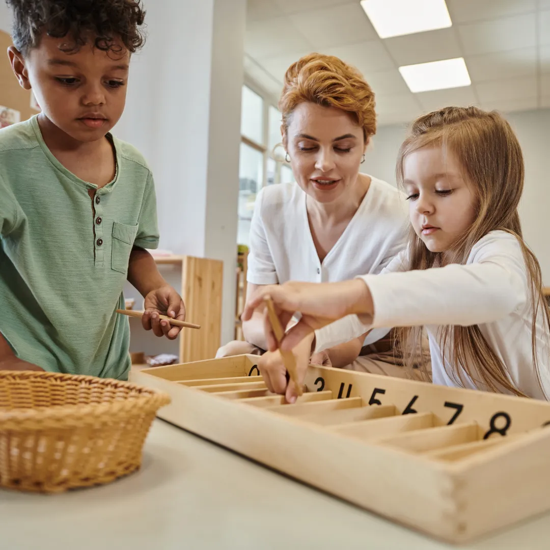 Eine Erzieherin hilft zwei Kindern bei einem Lernspiel in einer Kita.
