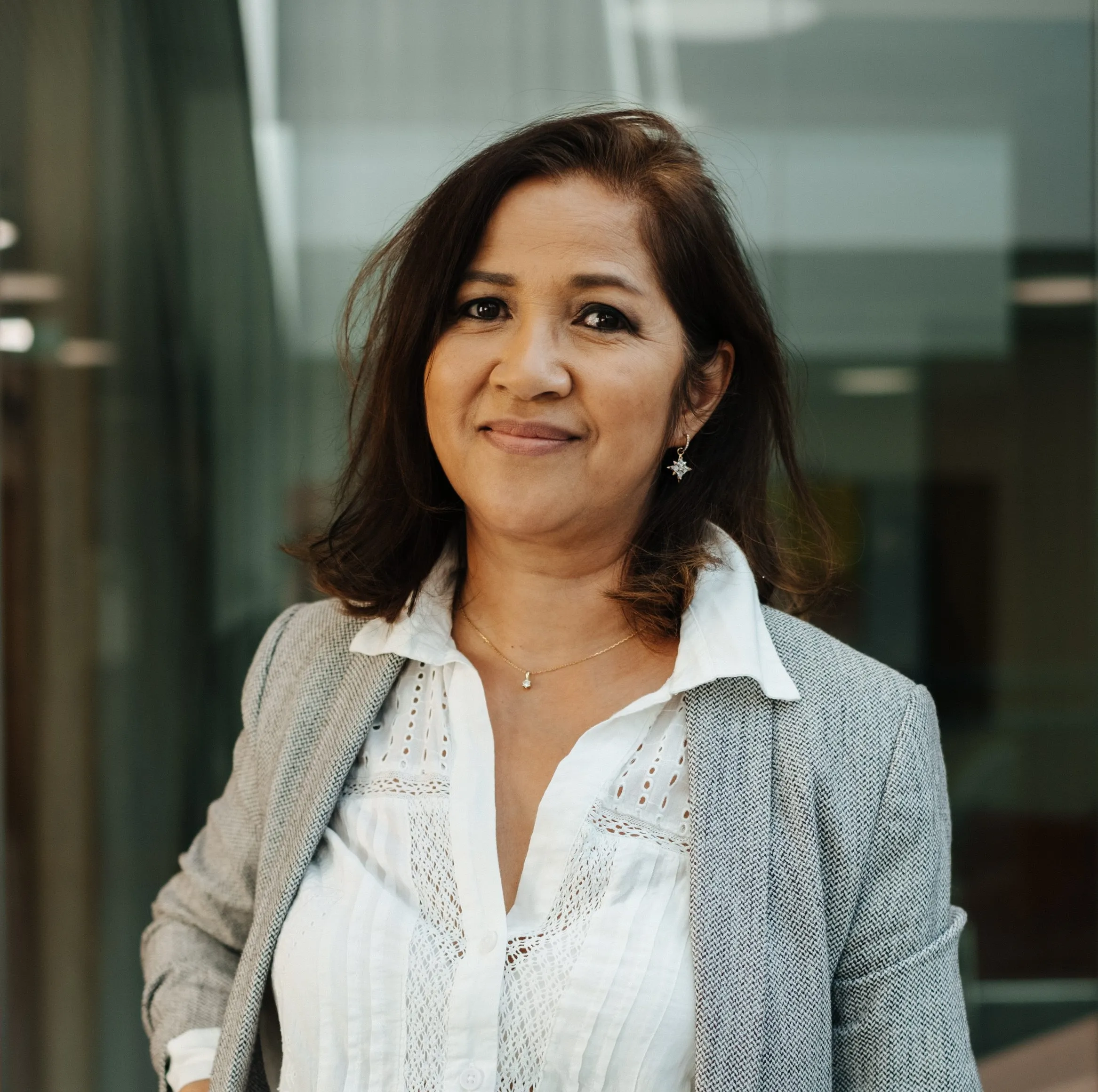 Eine Frau mit kurzen Haaren und Brille lächelt in die Kamera, umgeben von roten Blumen im Freien.