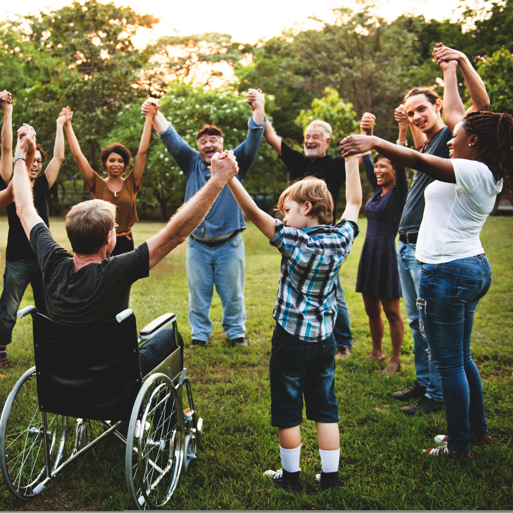 Eine Gruppe von Menschen, darunter ein Rollstuhlfahrer und ein Kind, hält sich im Freien an den Händen und bildet einen Kreis.