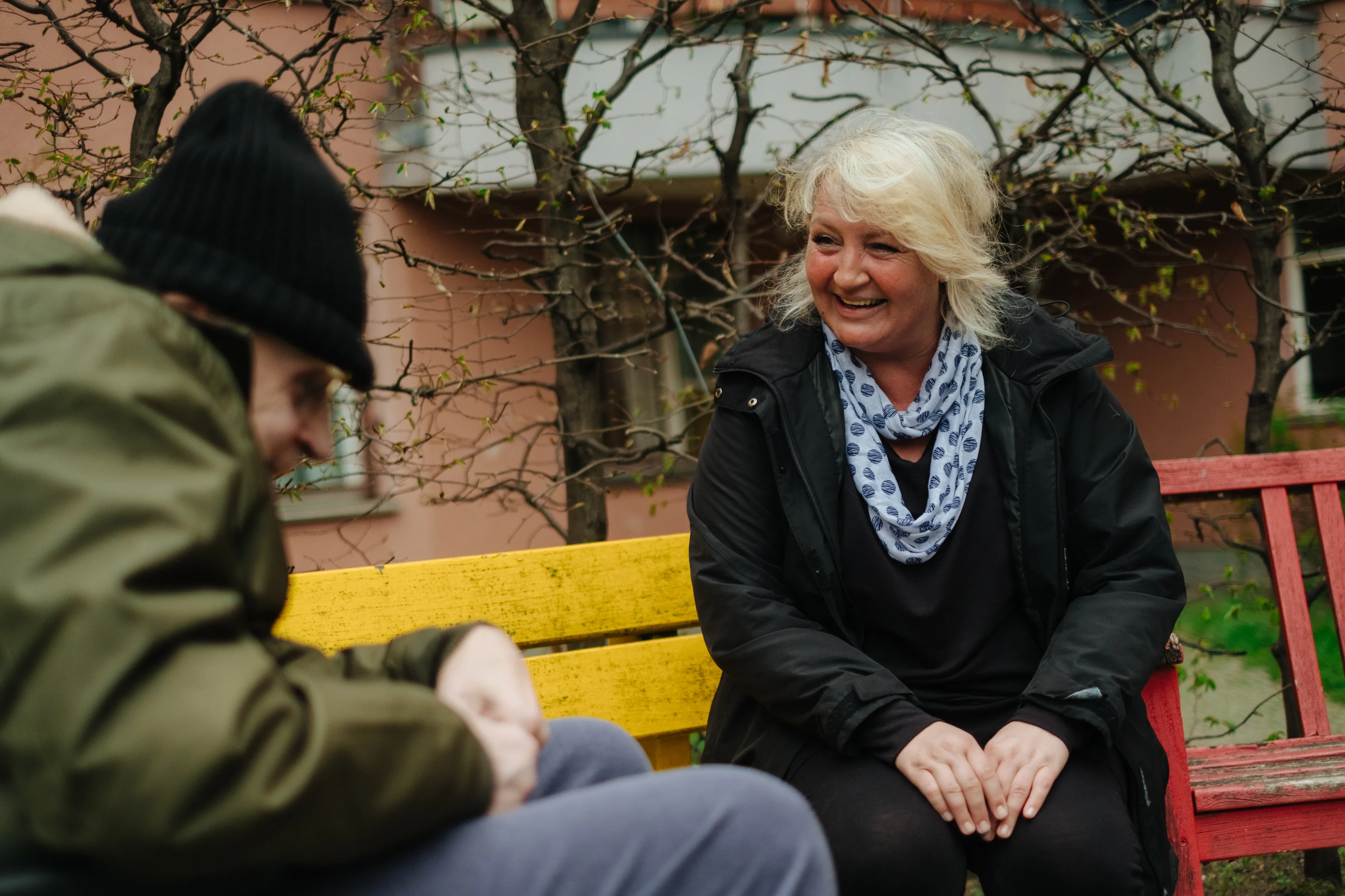 Eine lächelnde Pflegerin sitzt mit einem Mann auf einer Bank im Freien.