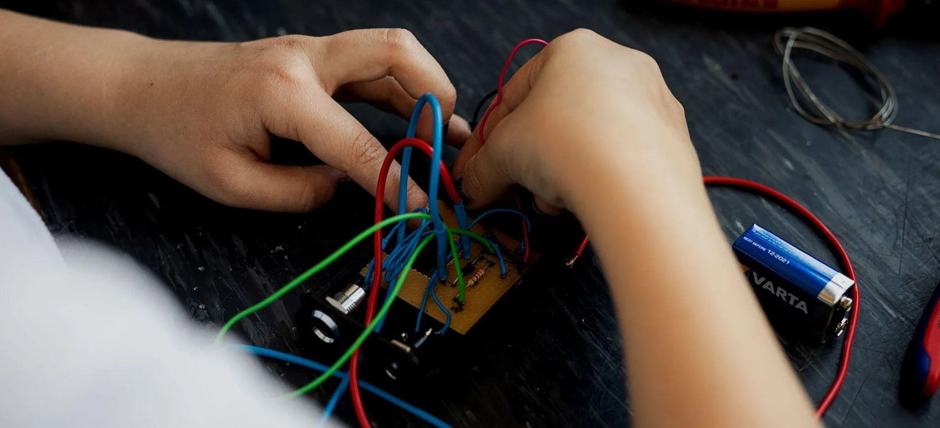 Du verbindest bunte Kabel auf einer Platine und arbeitest an einem Elektronikprojekt für den Bereich Verkehrstechnik.