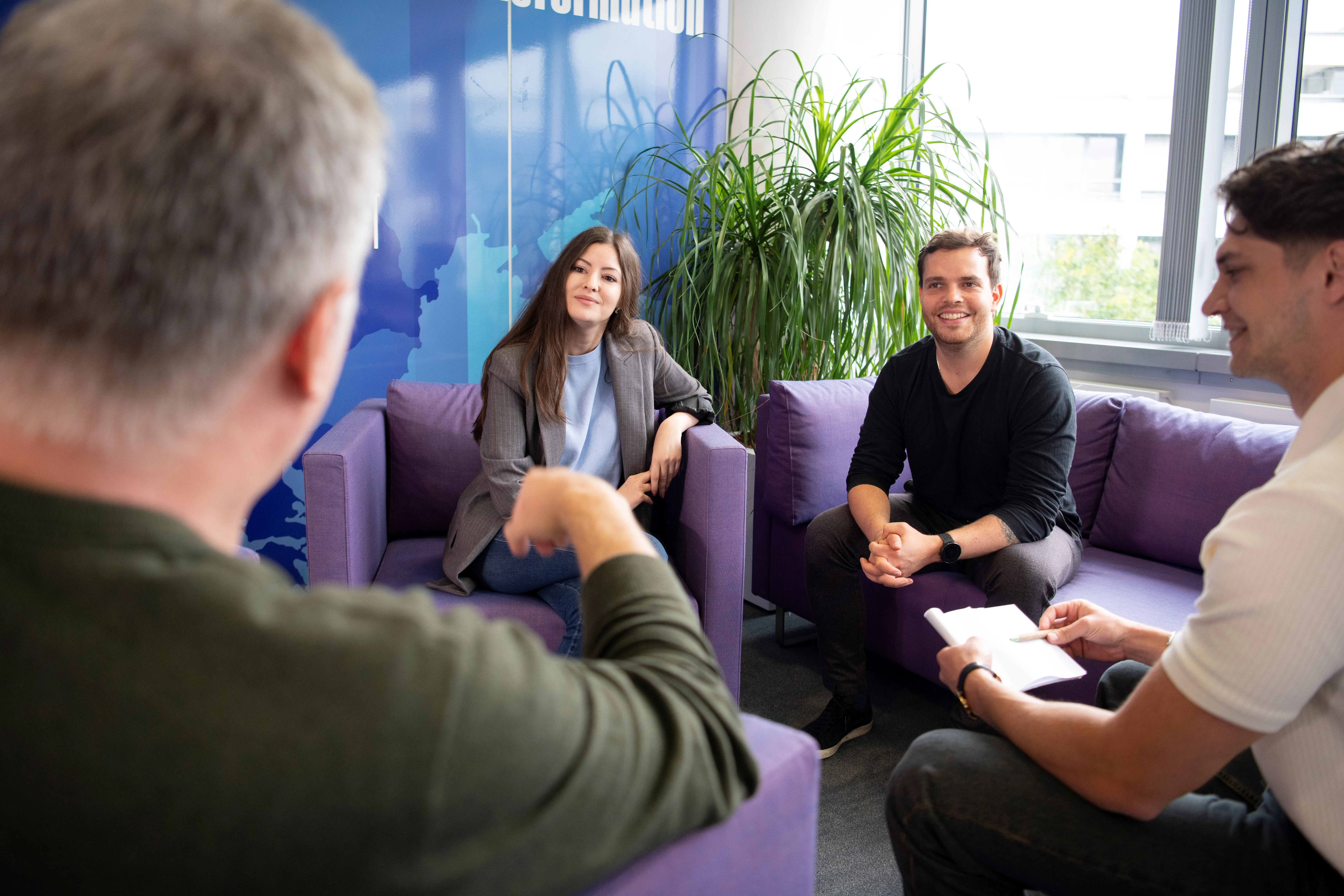 A laid-back team chat at Vantage Towers AG, with colleagues sharing ideas on comfy purple sofas in a bright office.