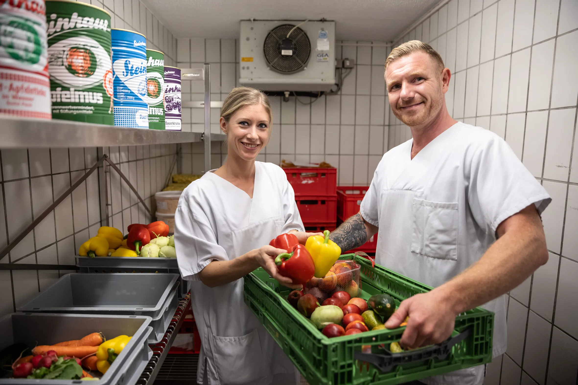 Zwei Vitos Service Mitarbeitende aus dem Catering in weißer Arbeitskleidung sortieren frisches Gemüse in einer Großküche.