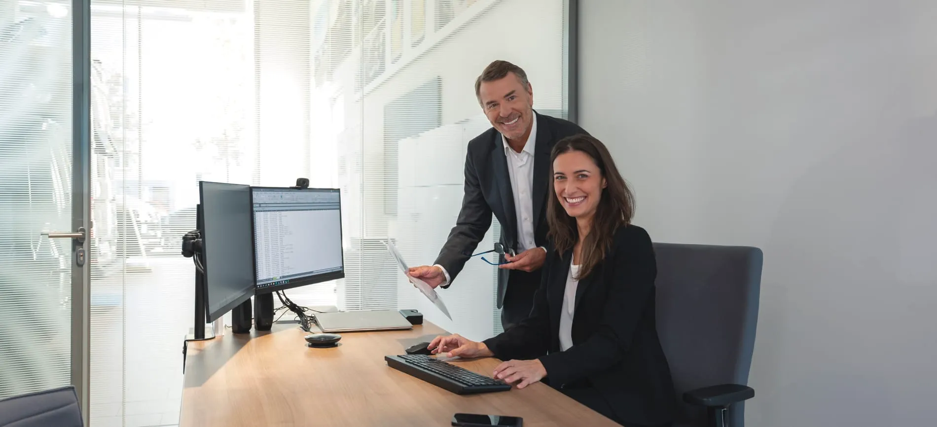 Zwei Personen in einem modernen Büro bei Volkswagen Retail GmbH; eine Frau arbeitet am Computer, ein Mann zeigt auf ein Dokument.