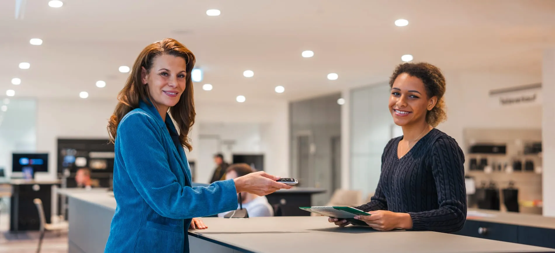 Zwei Frauen im Volkswagen-Autohaus, eine übergibt der anderen einen Autoschlüssel an einem Tresen.