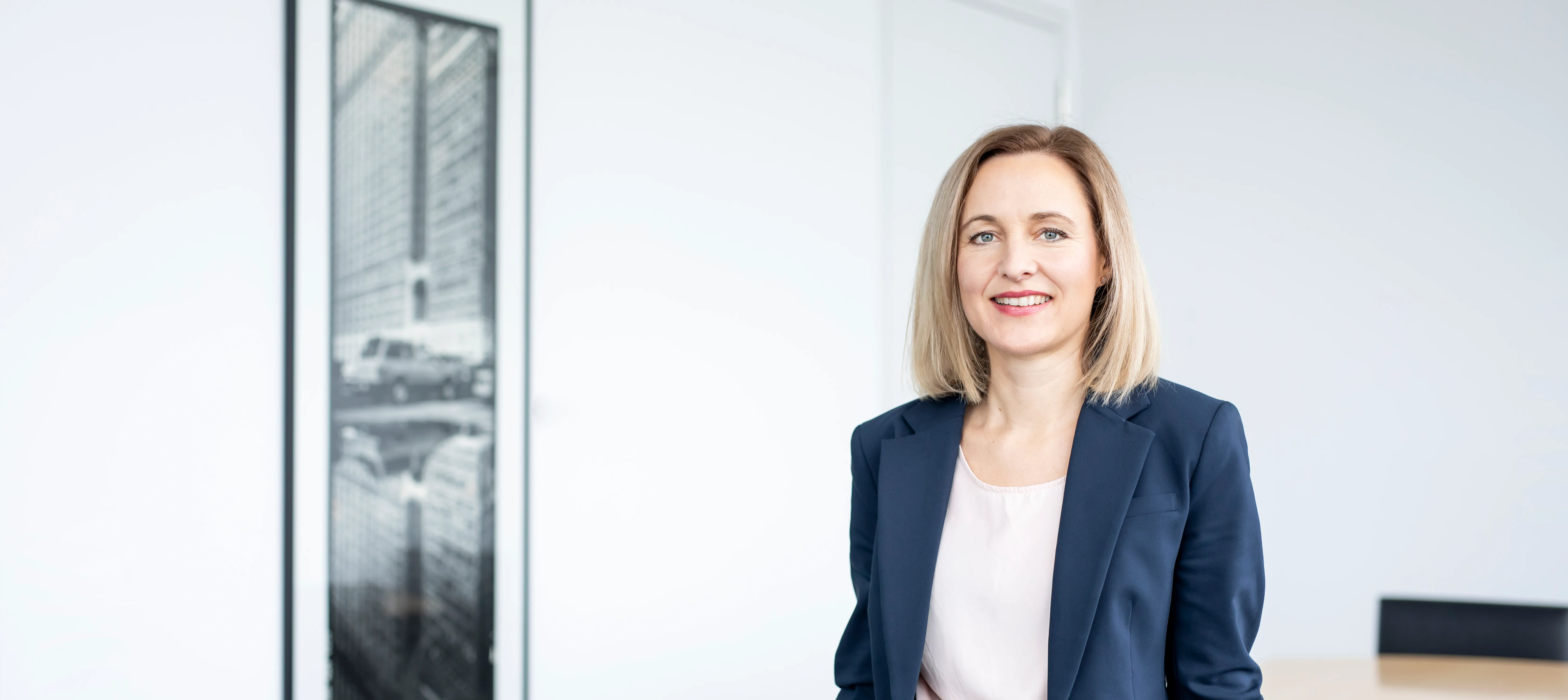 Freundliche Bankmitarbeiterin im Business-Outfit lächelt in modernem Büro der VR Bank.