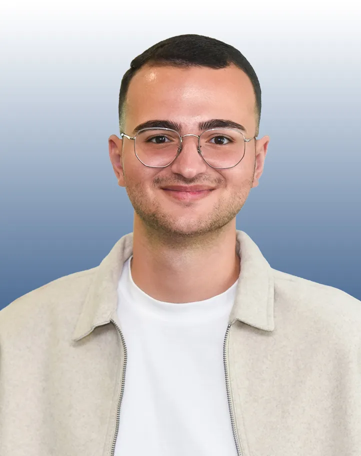 Junger Mann mit Brille und hellem Pullover lächelt freundlich, steht vor blauem Hintergrund für deine Karriere bei VR Bank.