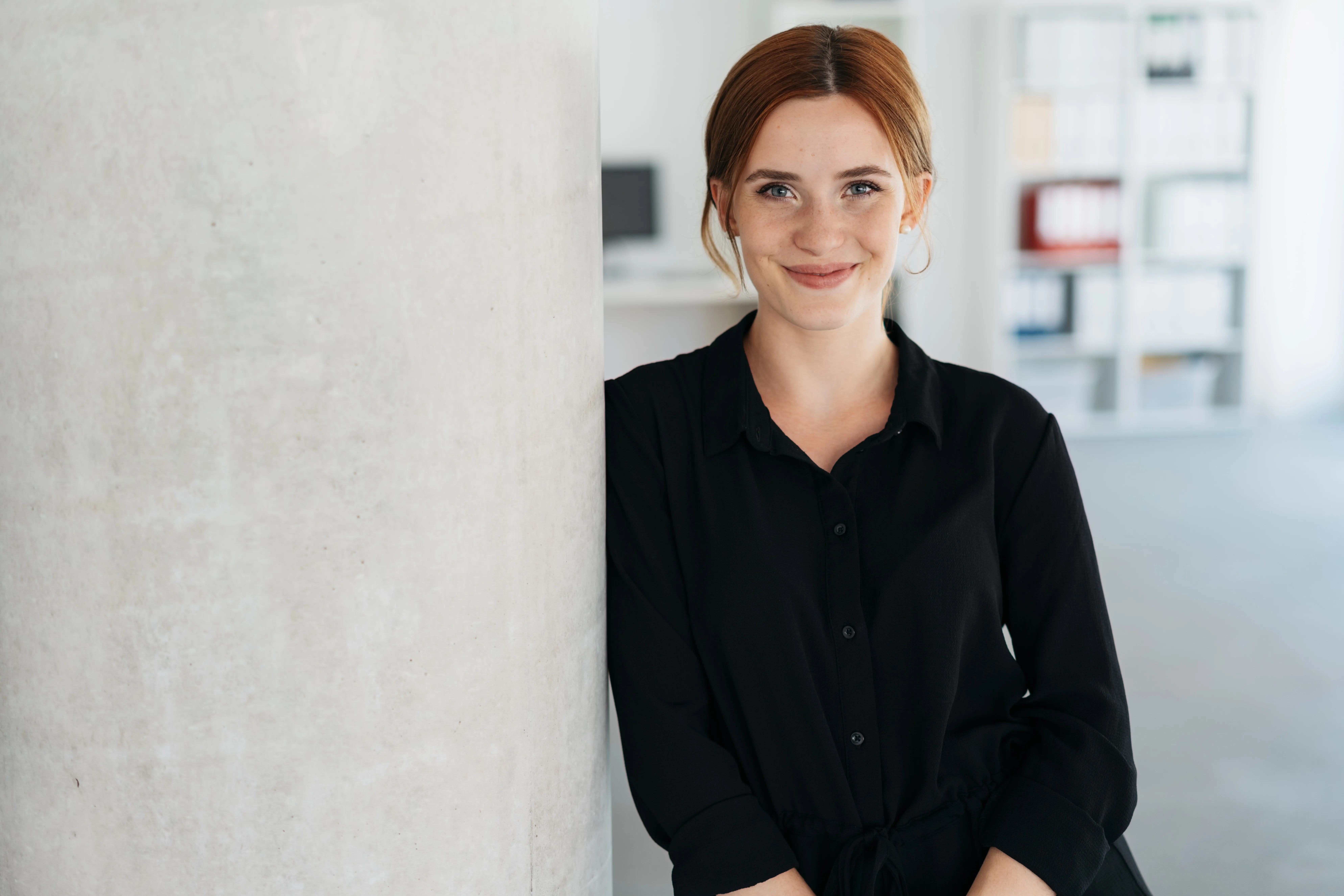 Junge Frau mit freundlichem Lächeln steht in modernem Büro, bereit für Deinen Karrierestart bei der VR Bank.