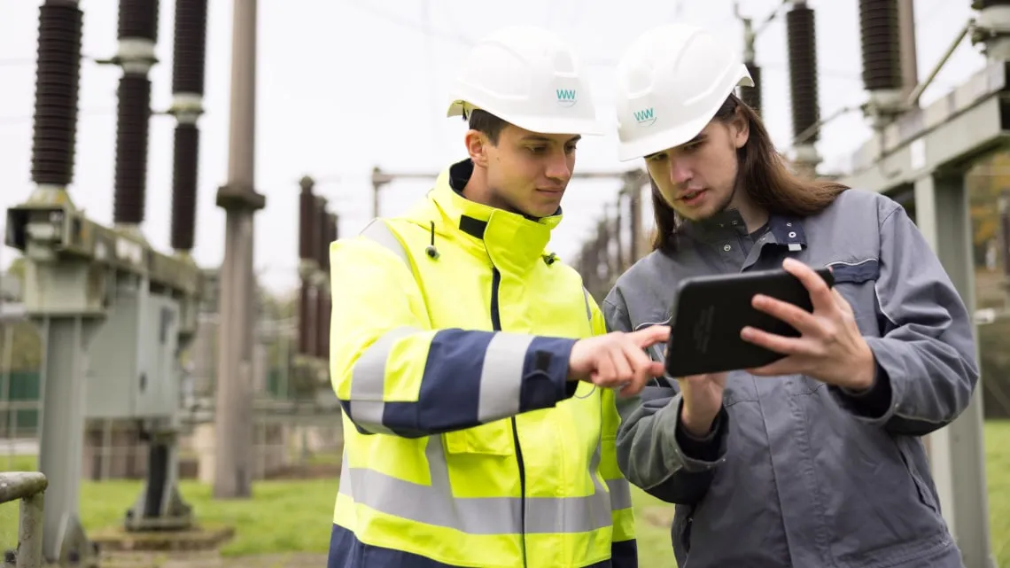 Zwei Mitarbeitende von Westfalen Weser Netz prüfen gemeinsam Daten auf einem Tablet im Umspannwerk.