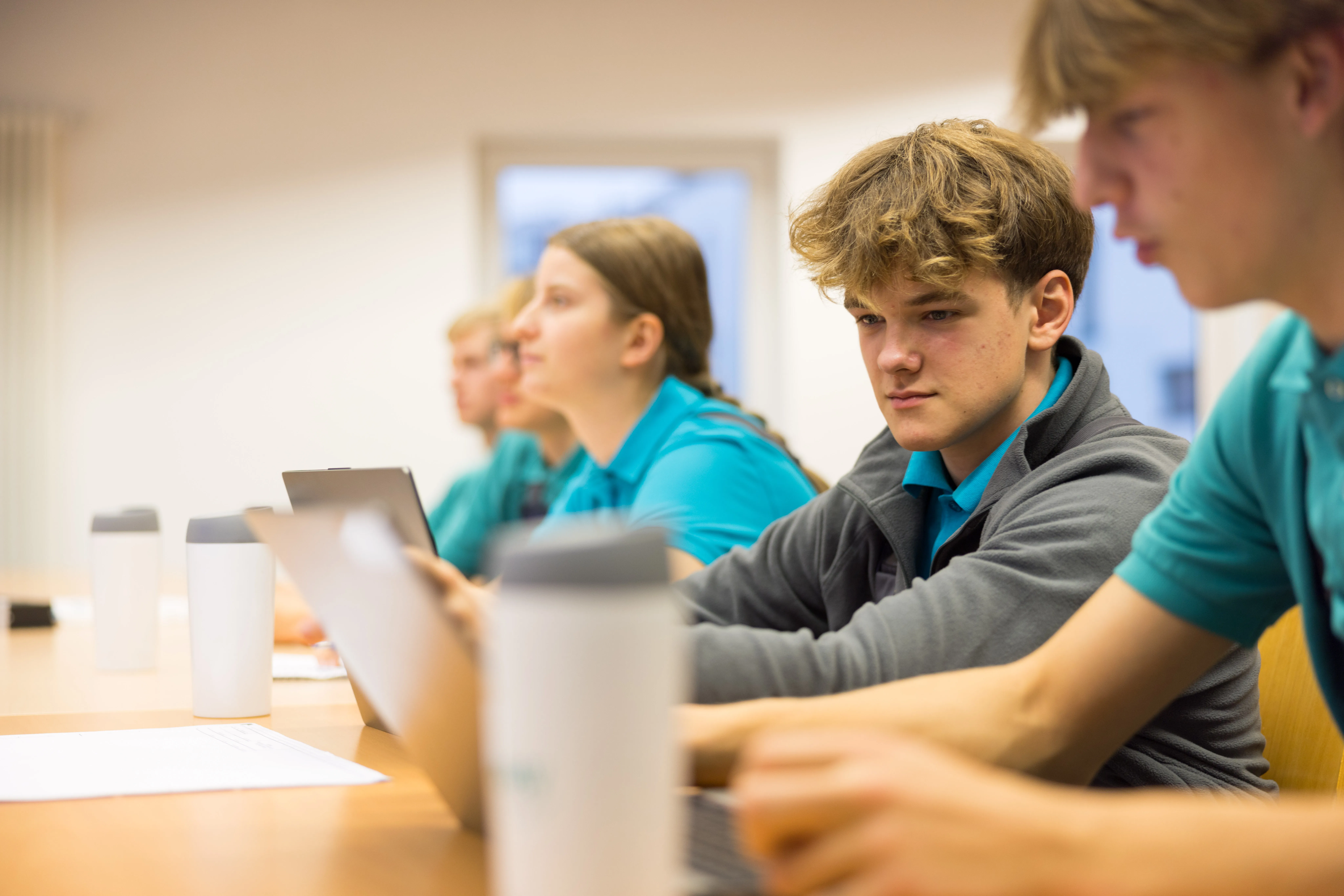 Junge Menschen in blauer Arbeitskleidung arbeiten gemeinsam an Laptops in einem Schulungsraum bei Westfalen Weser Netz.