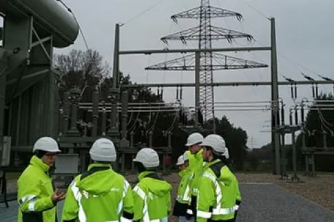 Personen in Sicherheitsausrüstung vor Strommast.