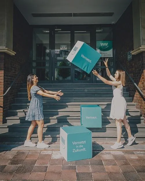 Zwei Frauen heben Boxen vor einem Gebäude.